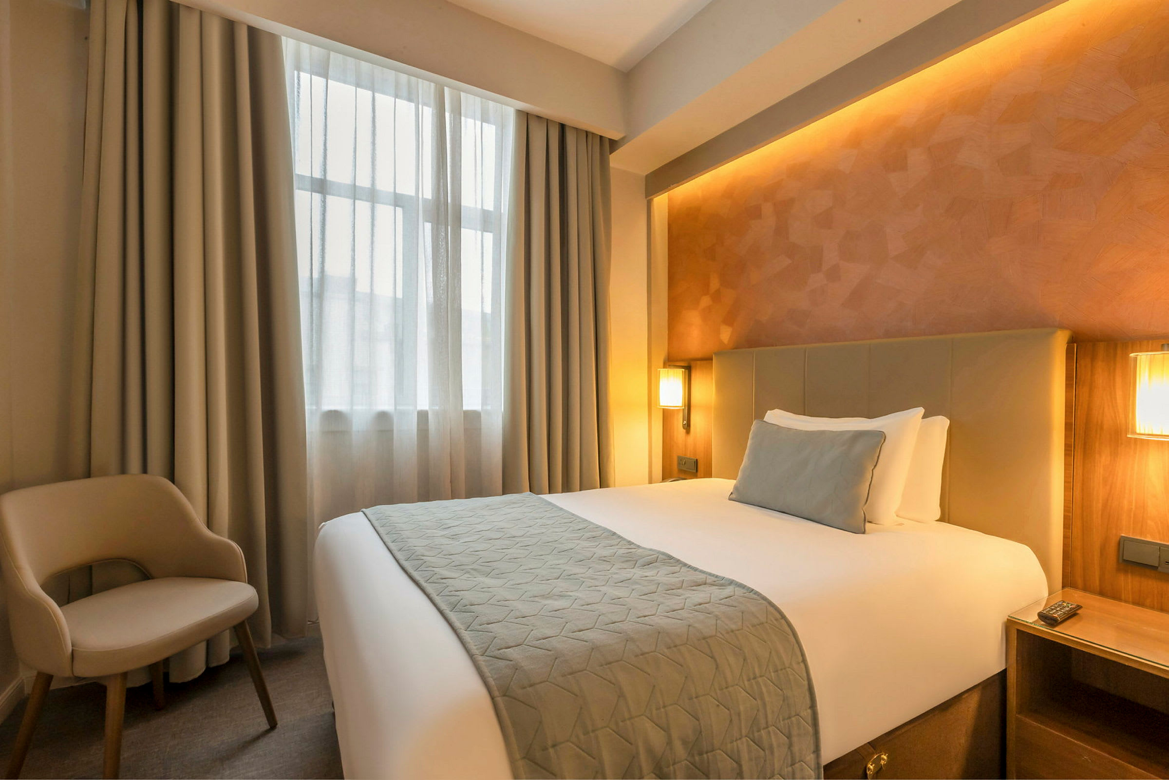Hotellihuone, jossa sänky, tuoli ja ikkuna verhoineen. (Tekoälyn luoma teksti)