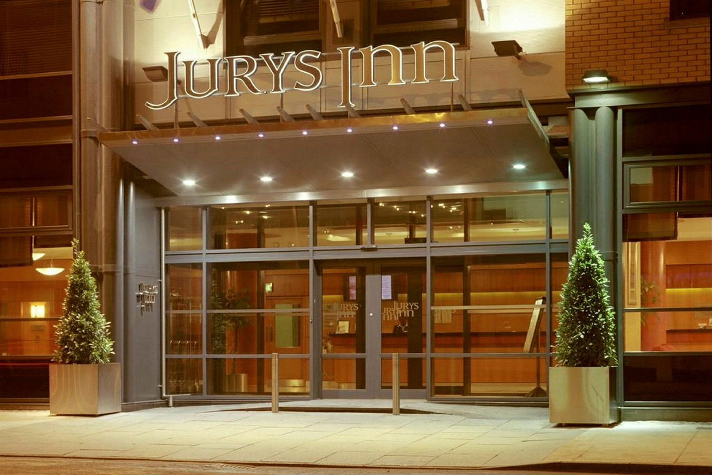 Hotellin sisäänkäynti, jossa lasiovet ja yläpuolella 'Jurys Inn' -kyltti. (Tekoälyn luoma teksti)