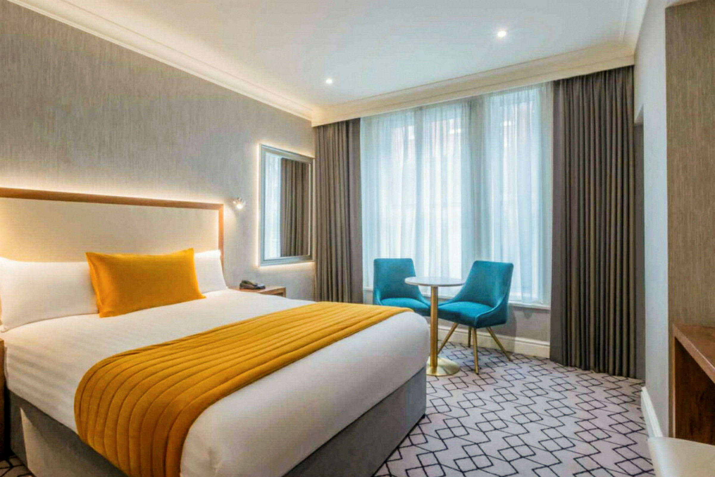 Hotellihuone, jossa on parivuode, kaksi sinistä tuolia ja pieni pöytä ikkunan vieressä. (Tekoälyn luoma teksti)