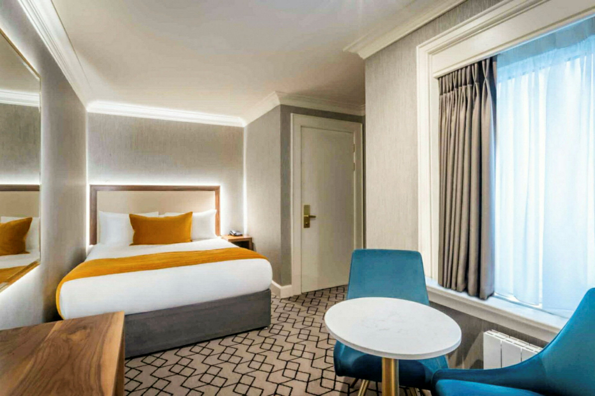 Hotellihuone, jossa on sänky, kaksi tuolia ja pöytä sekä luonnonvaloa ikkunasta. (Tekoälyn luoma teksti)