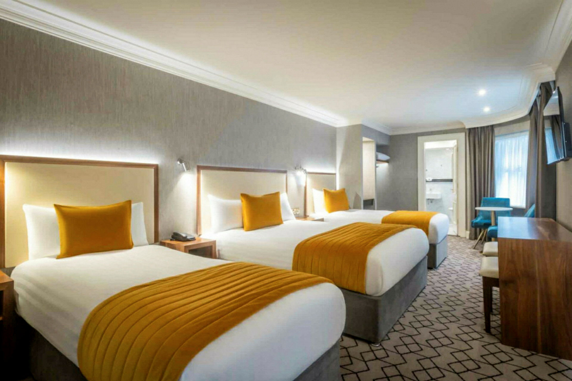 Hotellihuone, jossa on kolme vuodetta, oransseja yksityiskohtia ja kirjoituspöytä. (Tekoälyn luoma teksti)