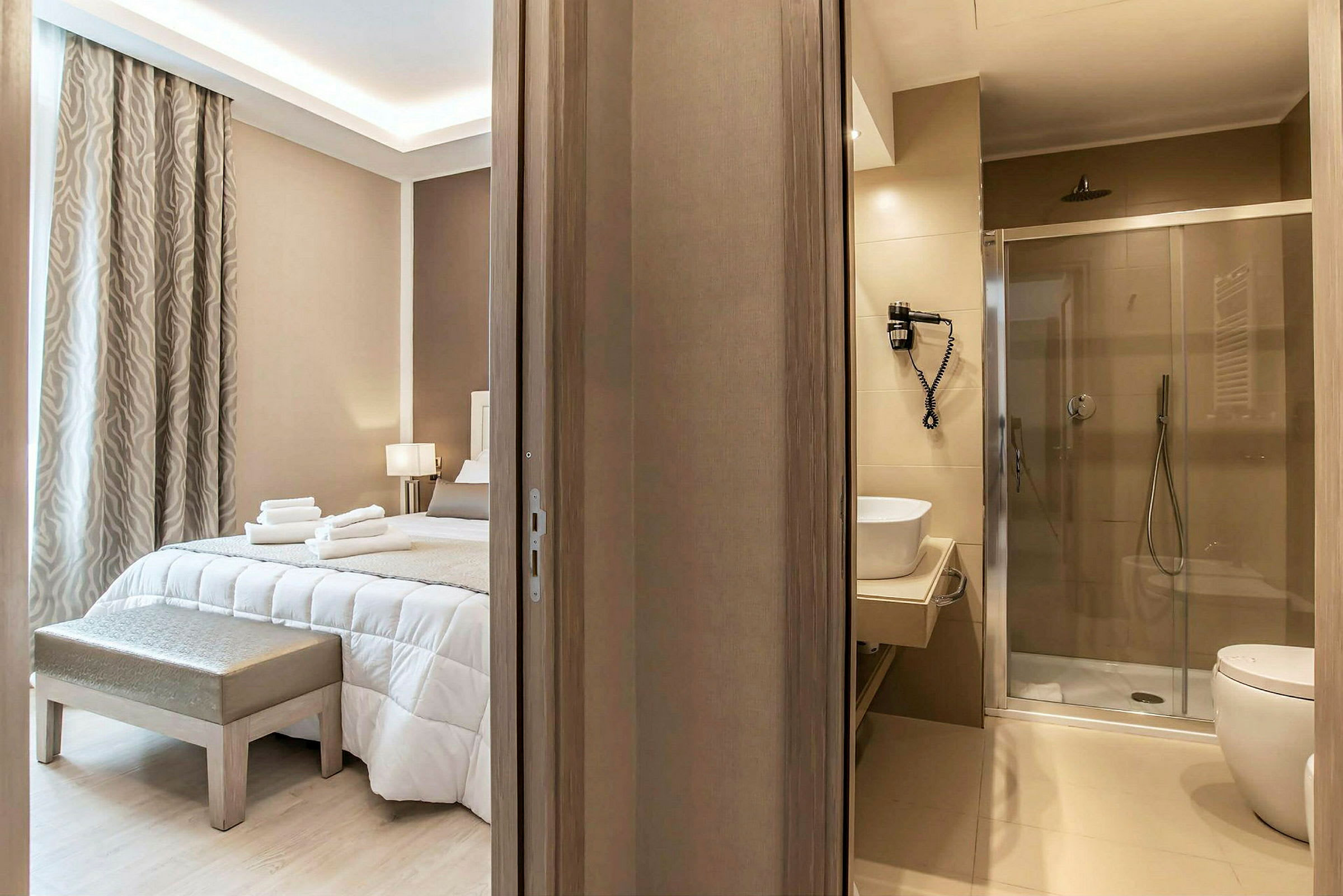 Hotellihuone, jossa leveä sänky, sisustettu vaaleilla sävyillä, modernin kylpyhuoneen vieressä. (Tekoälyn luoma teksti)