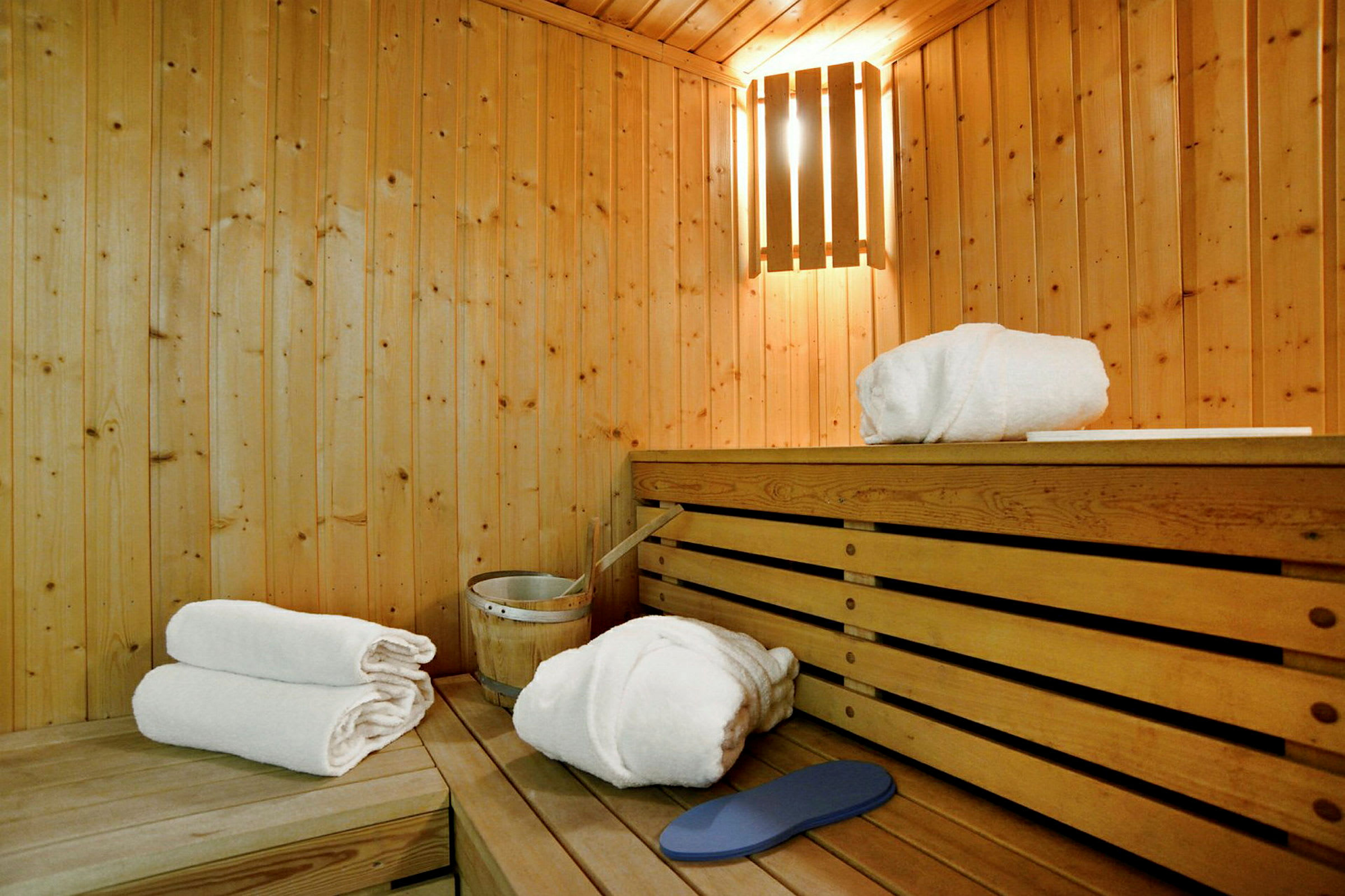 Sauna, jossa on puupaneelit ja himmeä valaistus. Puuistuimelle asetettu valkoisia pyyhkeitä sekä saunatarvikkeita. (Tekoälyn luoma teksti)