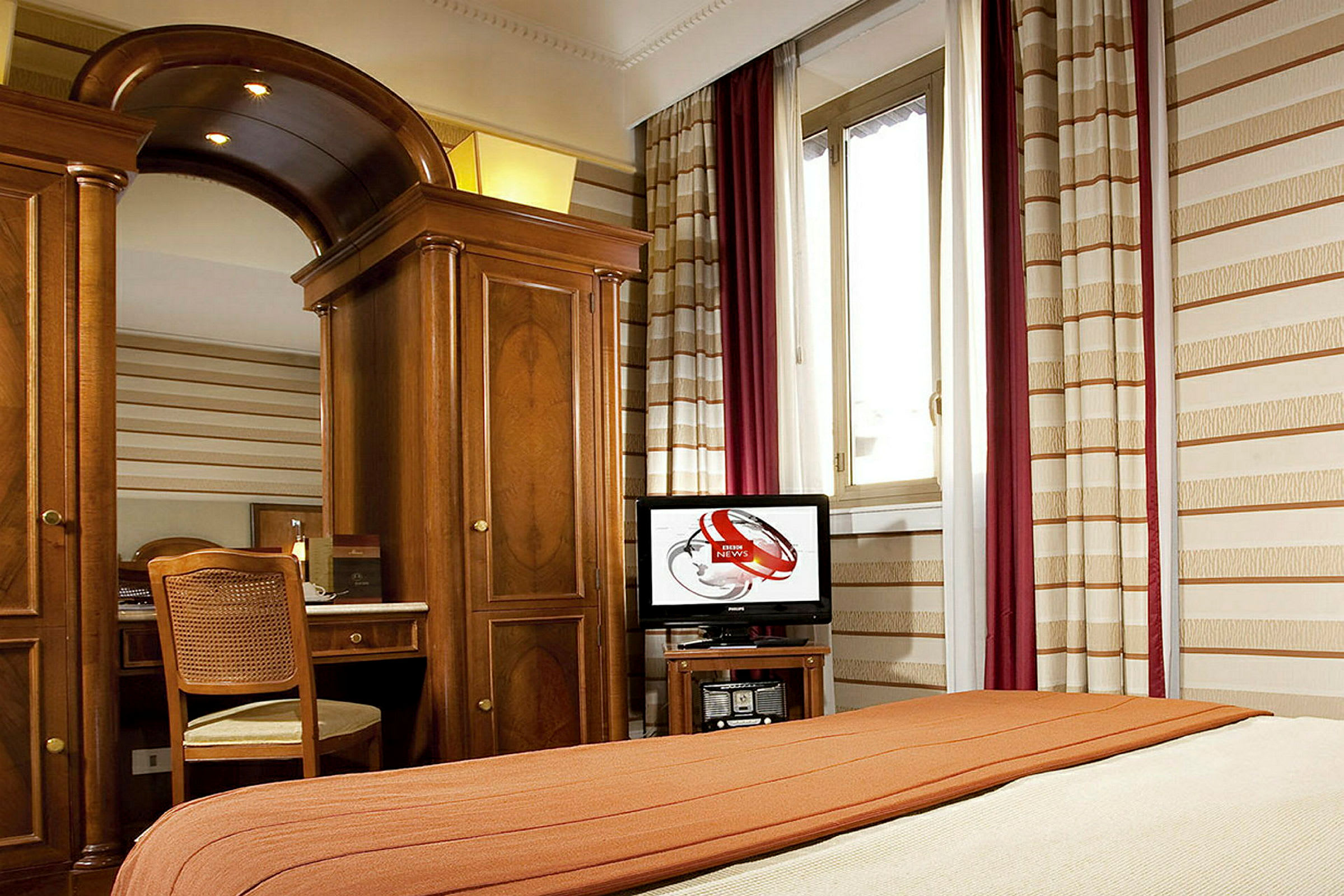 Hotellihuone, jossa on sänky, puisia huonekaluja, peili, tuoli ja ikkuna. (Tekoälyn luoma teksti)