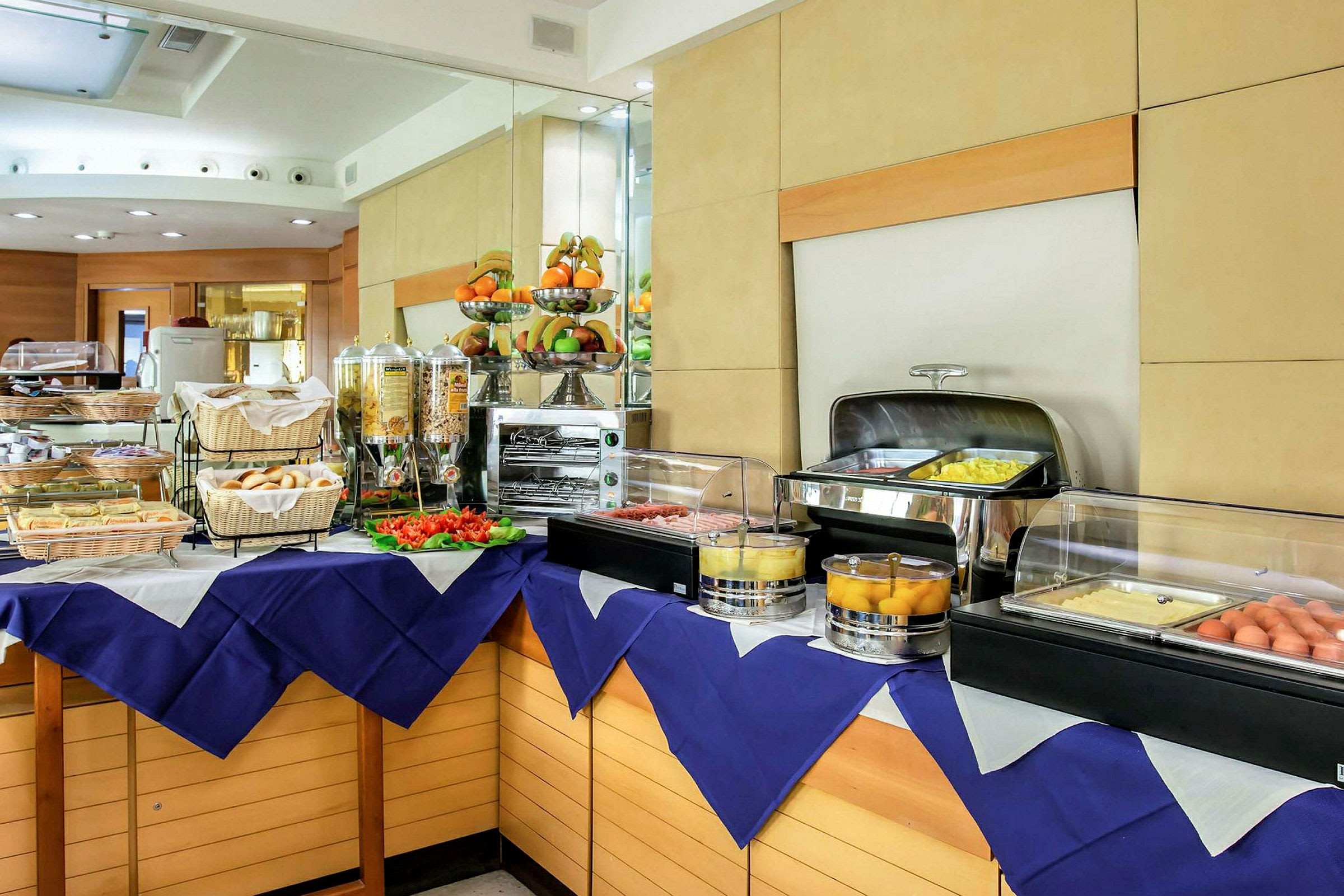 Buffet-pöytä, jossa on erilaisia ruokalajeja, mukaan lukien aamiaisvaihtoehtoja, kuten leipää, munia ja hedelmiä. (Tekoälyn luoma teksti)