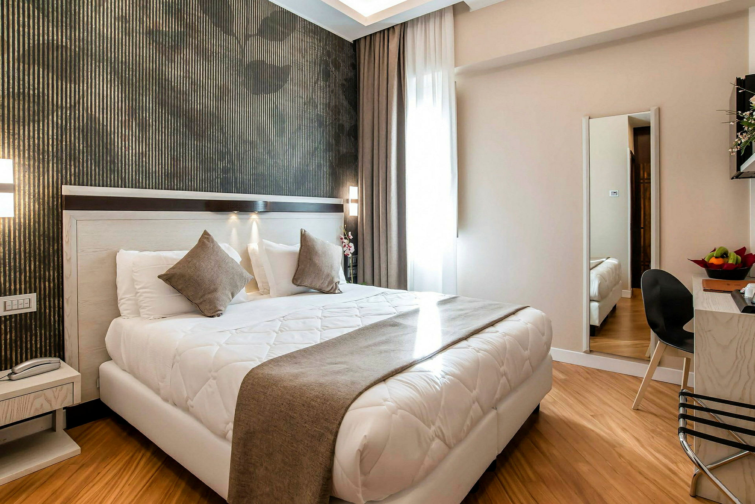 Modernisti sisustettu hotellihuone, jossa on parivuode, yöpöytä, peili ja oleskelualue. (Tekoälyn luoma teksti)