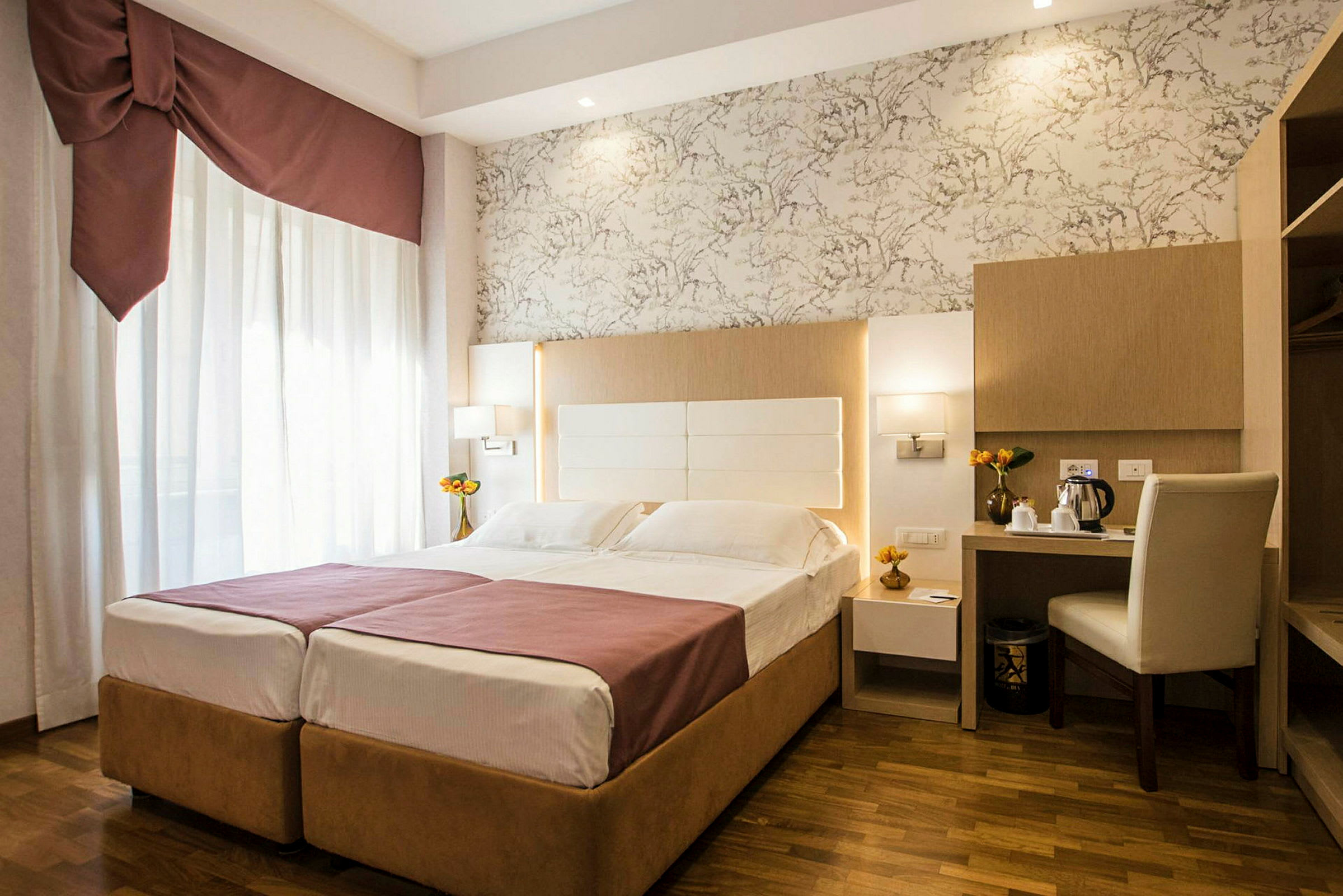 Hotellihuone, jossa on parivuode, työpöytä ja tuoli sekä koristeellisia yksityiskohtia. (Tekoälyn luoma teksti)