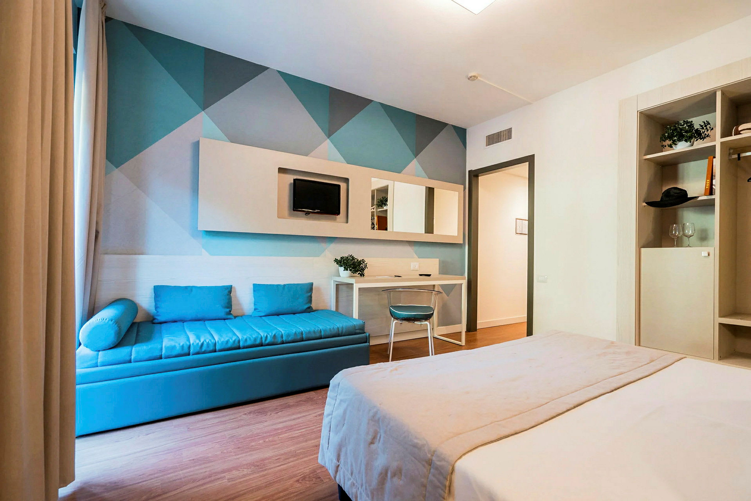 Hotellihuone, jossa on parivuode, sininen sohva ja kirjoituspöytäkulma. (Tekoälyn luoma teksti)