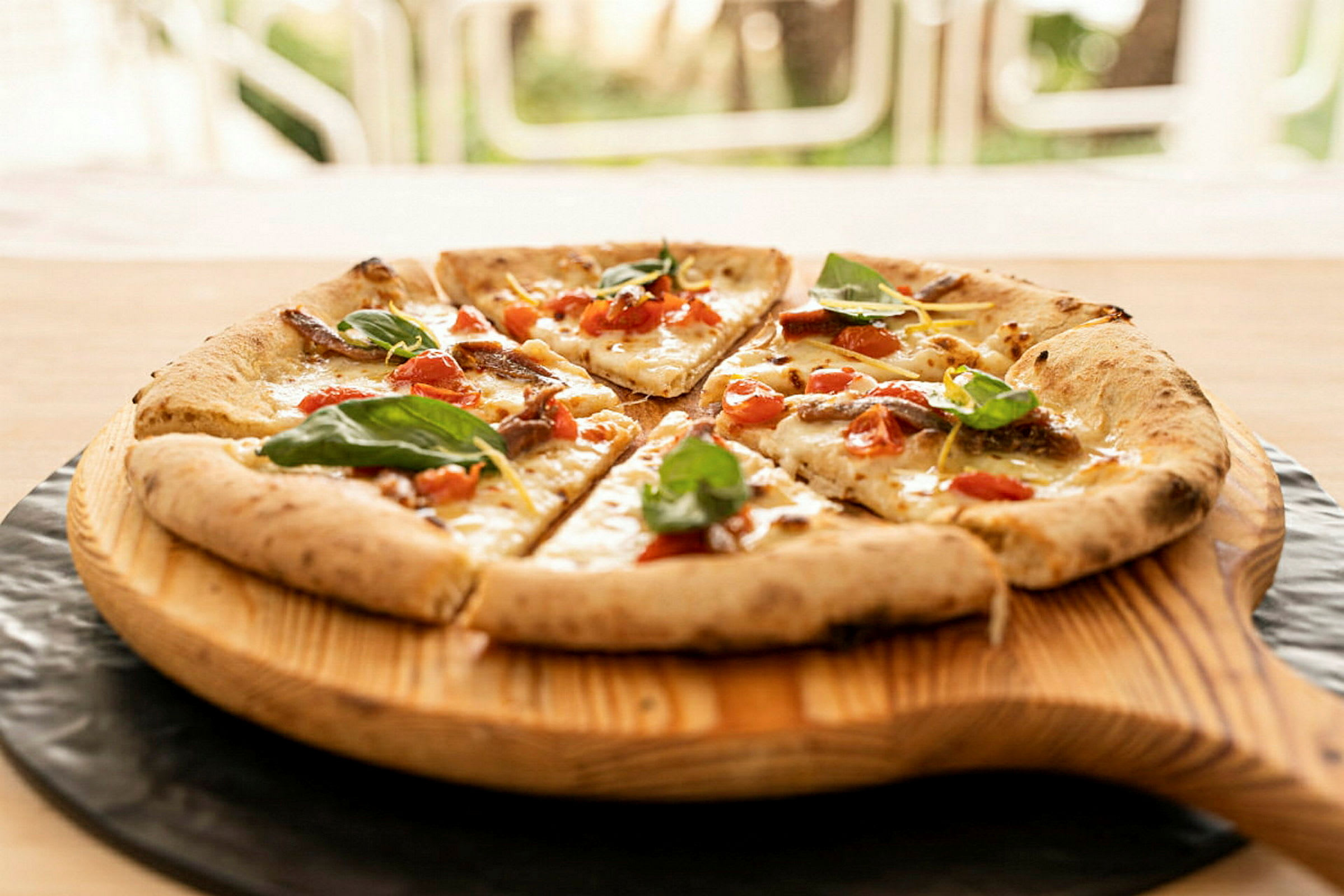 Pizza, jossa on tomaattia, juustoa ja lehtimausteita, tarjoillaan puulautasella. (Tekoälyn luoma teksti)