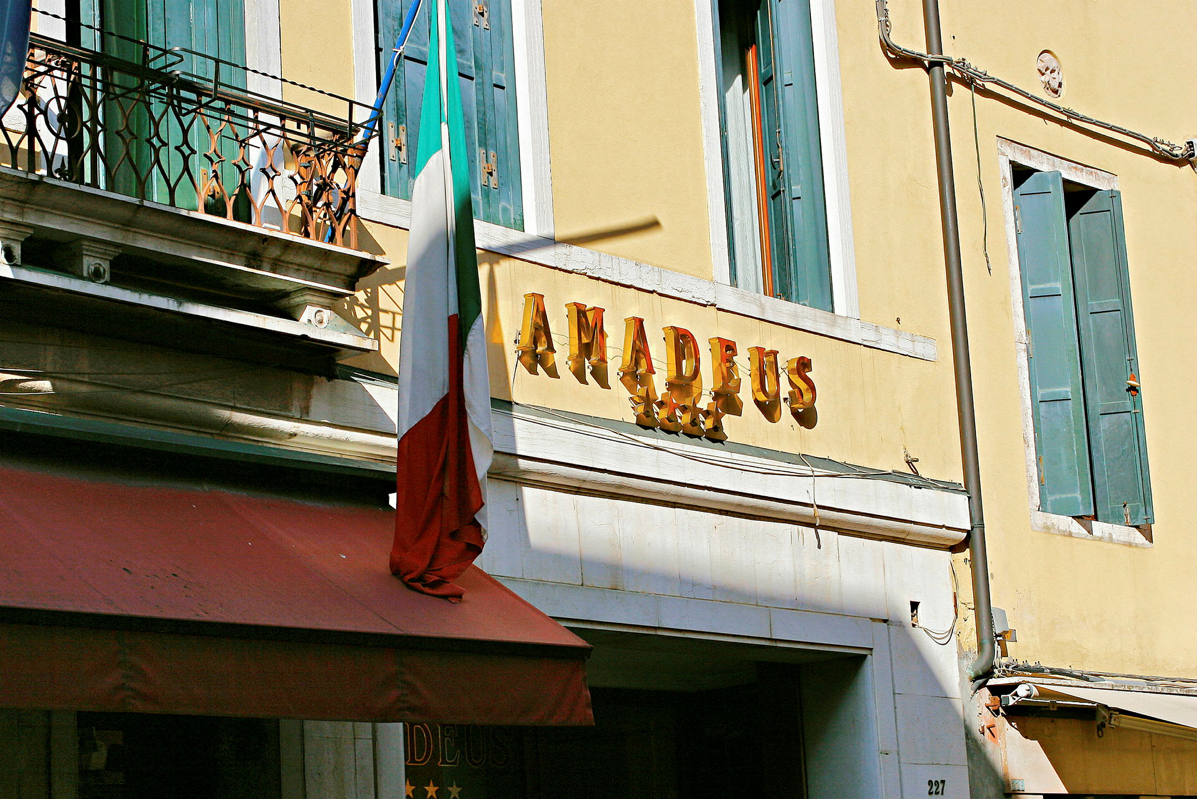 Hotellin julkisivu, jossa kyltti ”Amadeus” ja Italian lippu. (Tekoälyn luoma teksti)