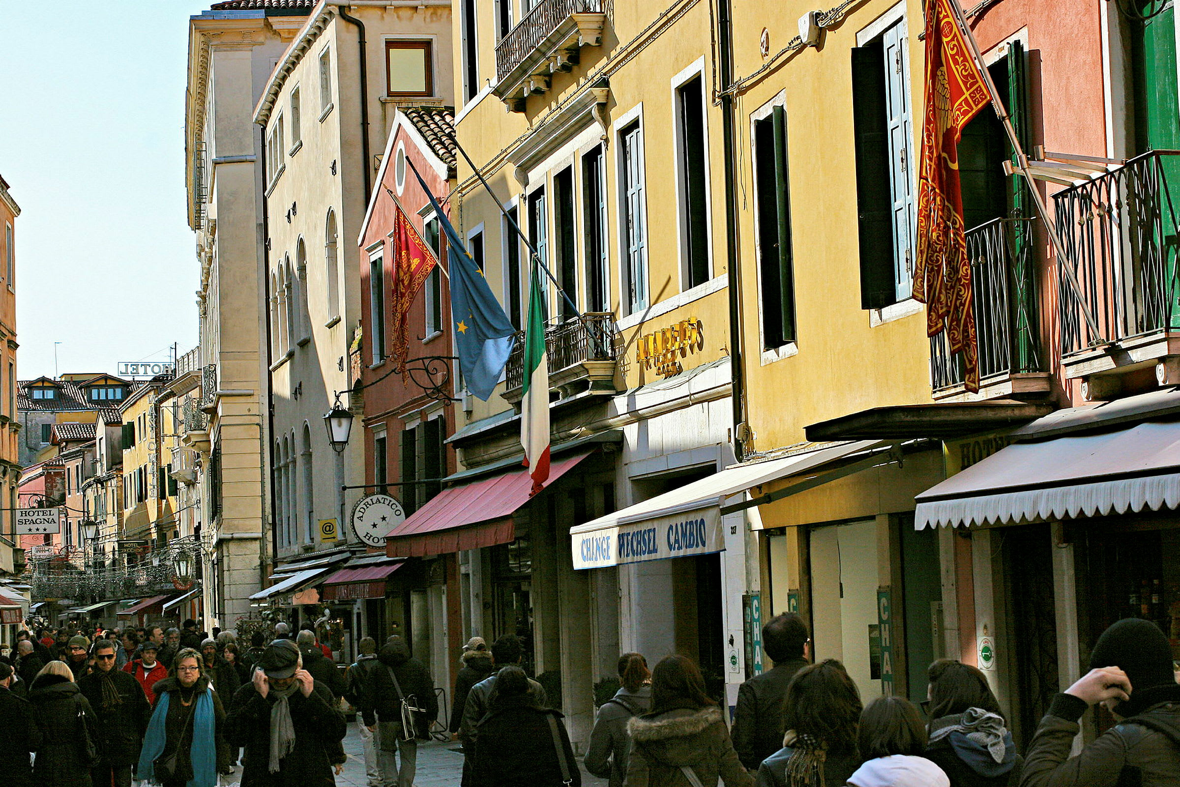 Vilkas katu, jota reunustavat värikkäät rakennukset ja Italian sekä Euroopan liput, ympärillä kulkee ihmisiä. (Tekoälyn luoma teksti)