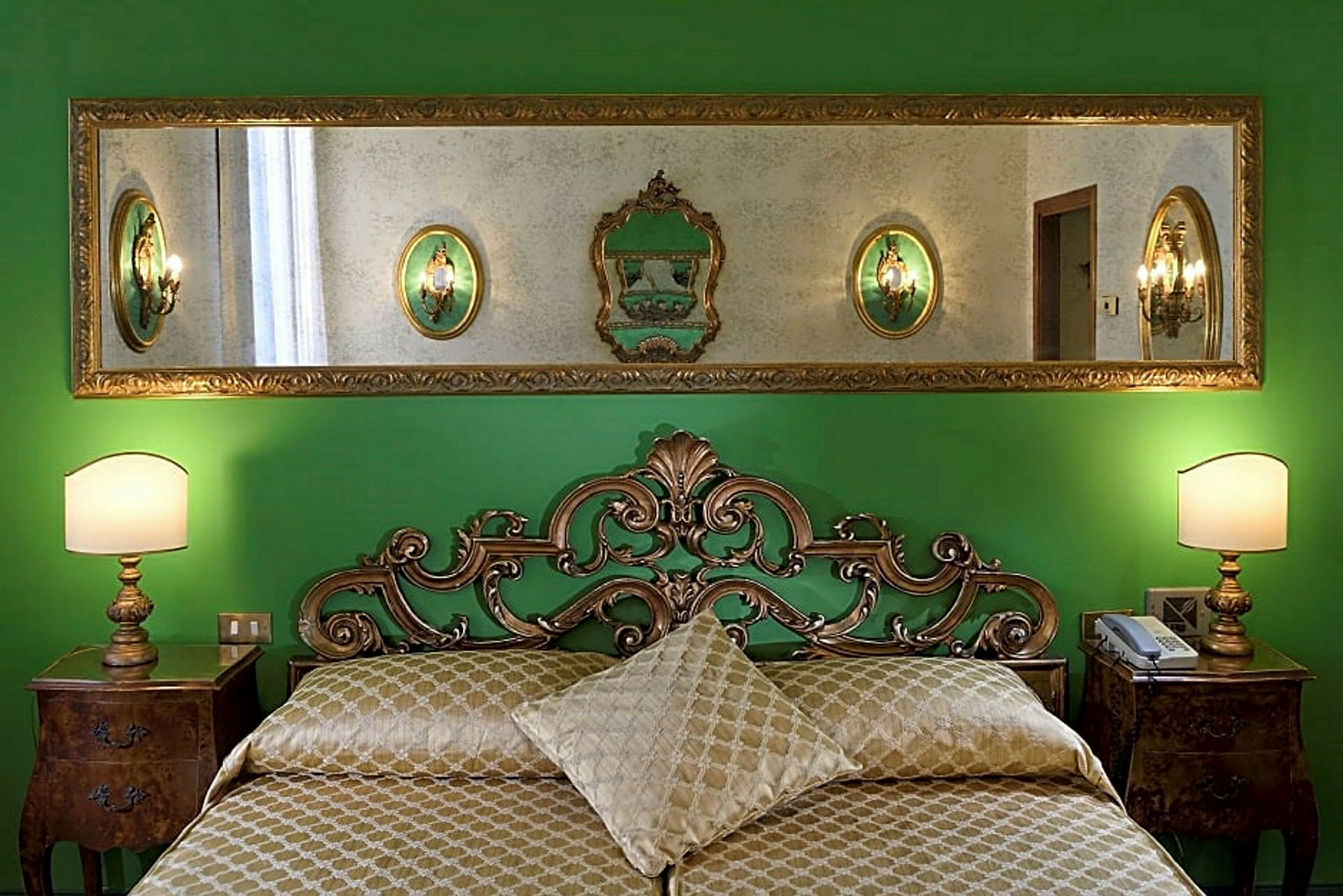 Makuuhuone, jossa on vihreät seinät, koristeltu kultainen sänkykehys ja peili sängyn yläpuolella. (Tekoälyn luoma teksti)