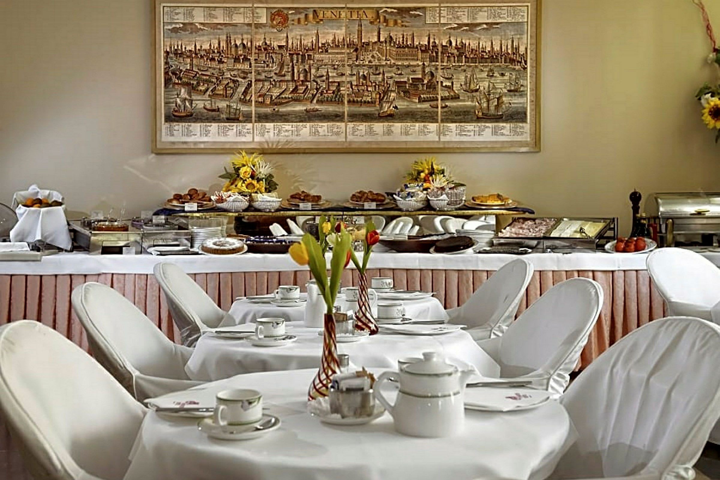 Aamiaispöytä, joka on katettu posliiniastioilla ja kukkakoristeluilla, edessä buffet, joka on täynnä ruokia. (Tekoälyn luoma teksti)