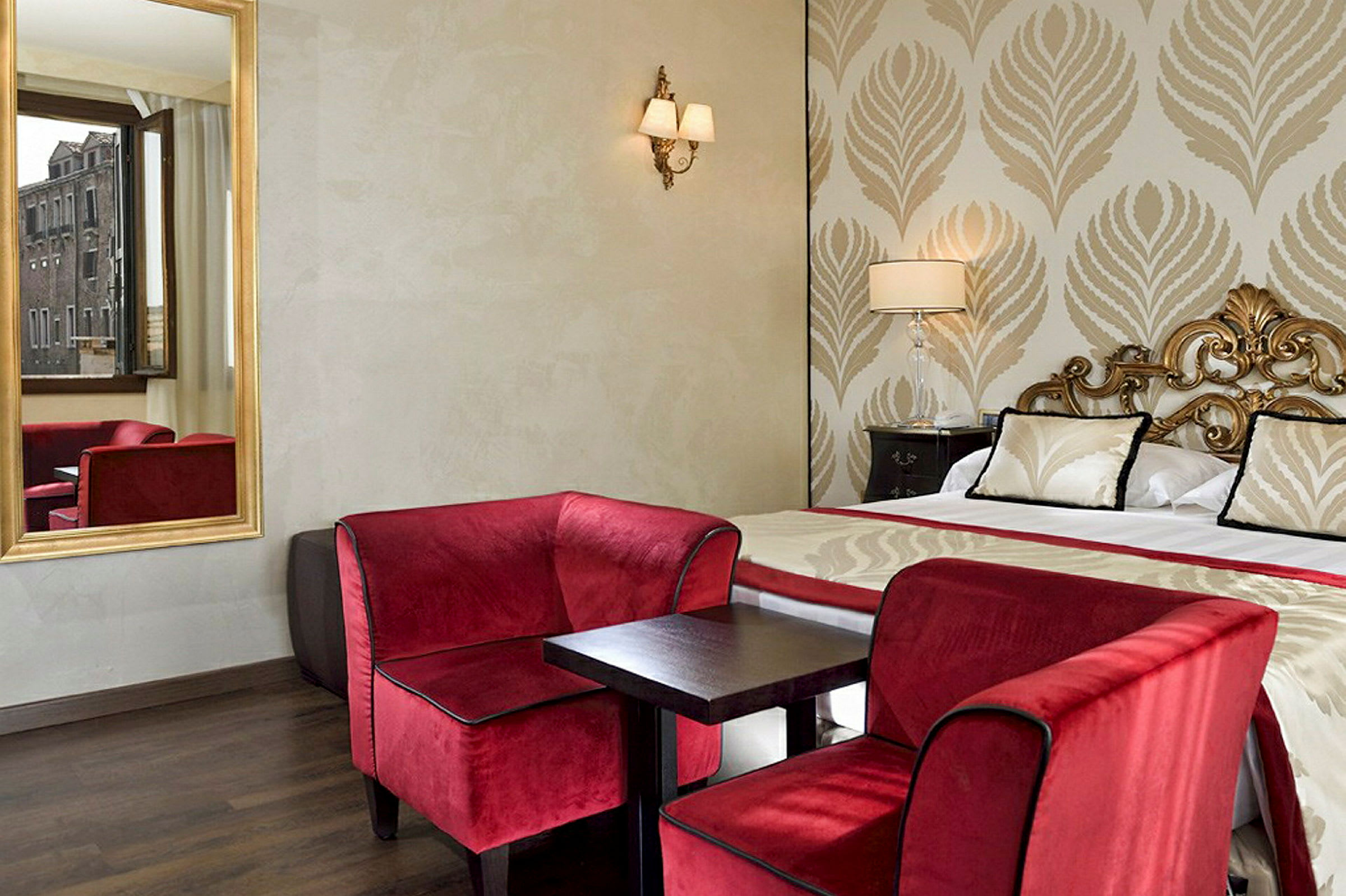 Tyylikäs hotellihuone, jossa on parisänky, punaiset nojatuolit ja pieni pöytä sekä ikkuna, josta on näkymä. (Tekoälyn luoma teksti)