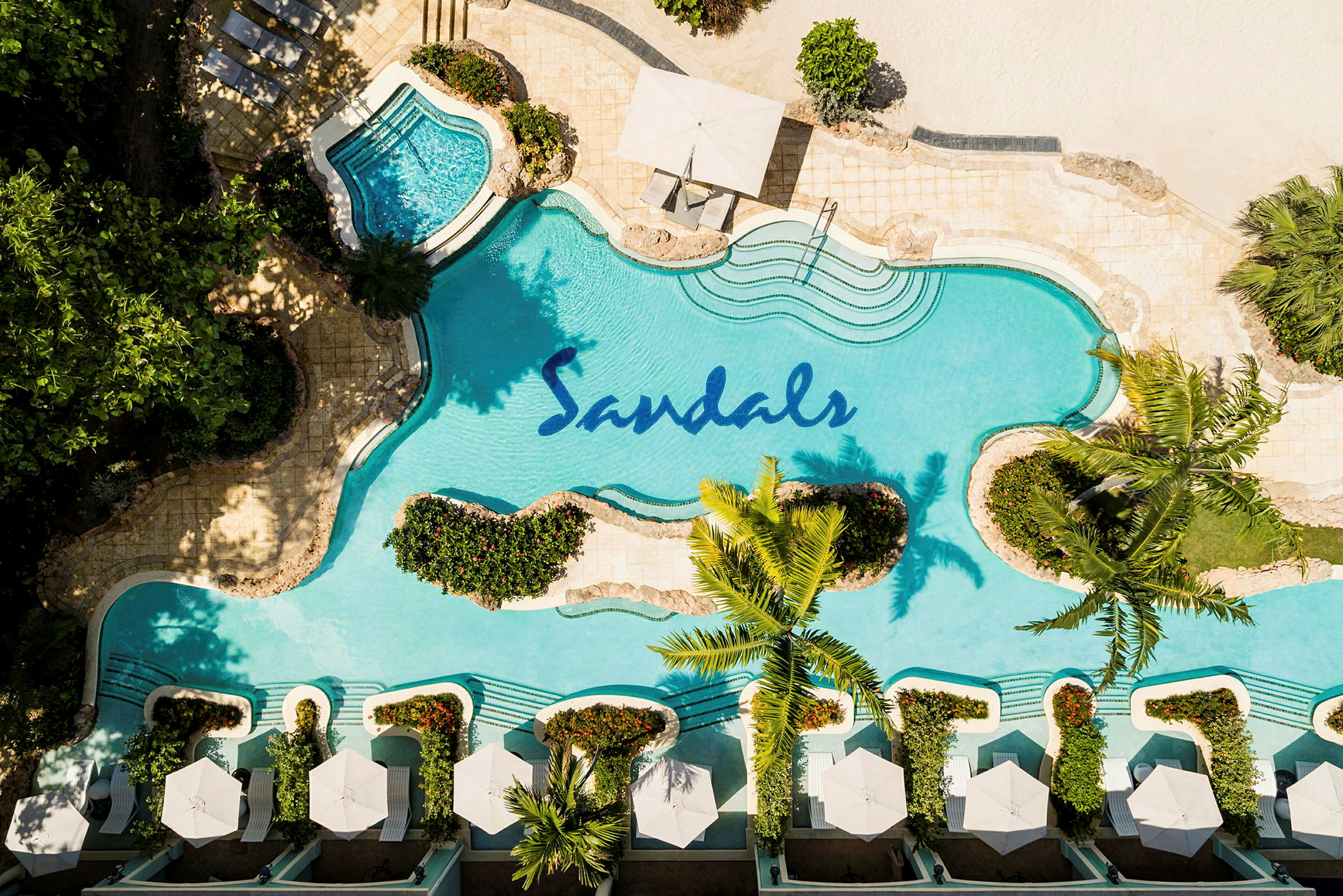 Lintuperspektiivi uima-altaasta, jossa Sandals-logo, ympäröity kasveilla ja aurinkotuoleilla, joissa on varjot. (Tekoälyn luoma teksti)