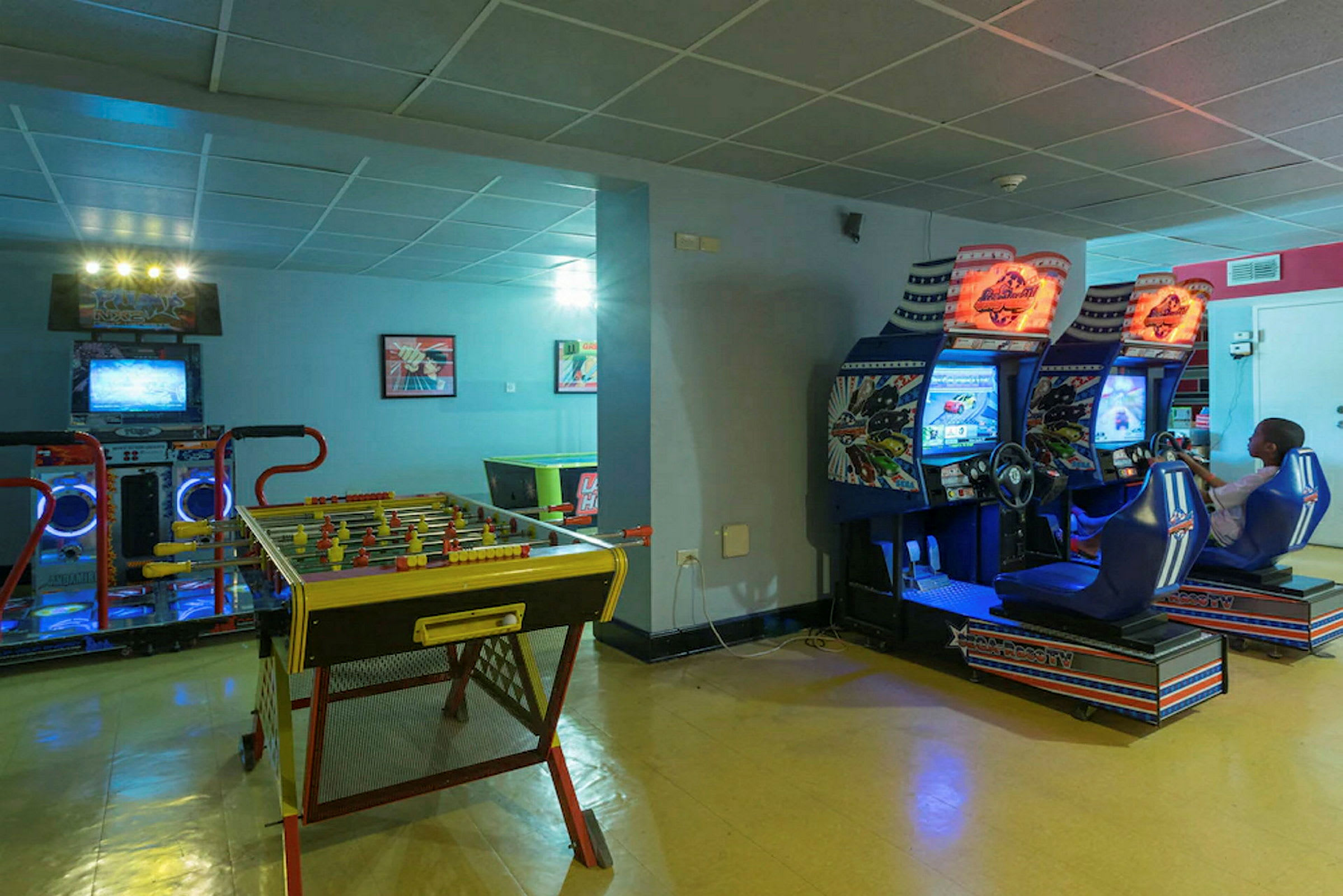 Huone, jossa on arcade-pelejä, mukaan lukien kilpa-ajopelejä sekä pöytäjalkapallopöytä. (Tekoälyn luoma teksti)