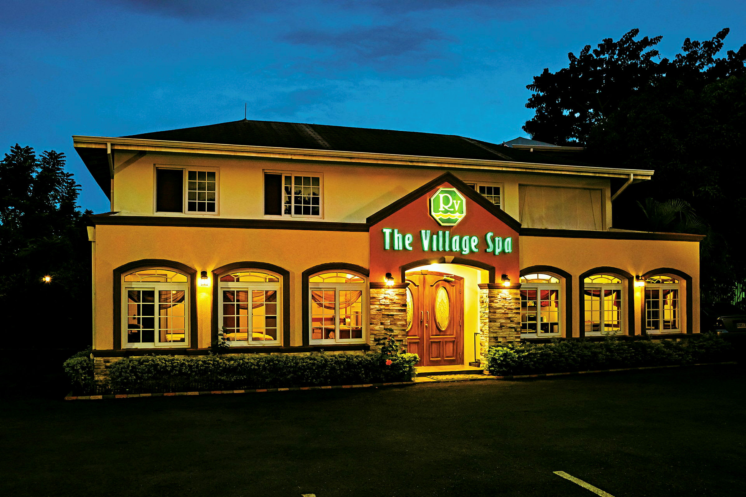 Kaksikerroksinen rakennus, valaistu julkisivu ja sisäänkäynti, jossa on kyltti nimeltä "The Village Spa". (Tekoälyn luoma teksti)