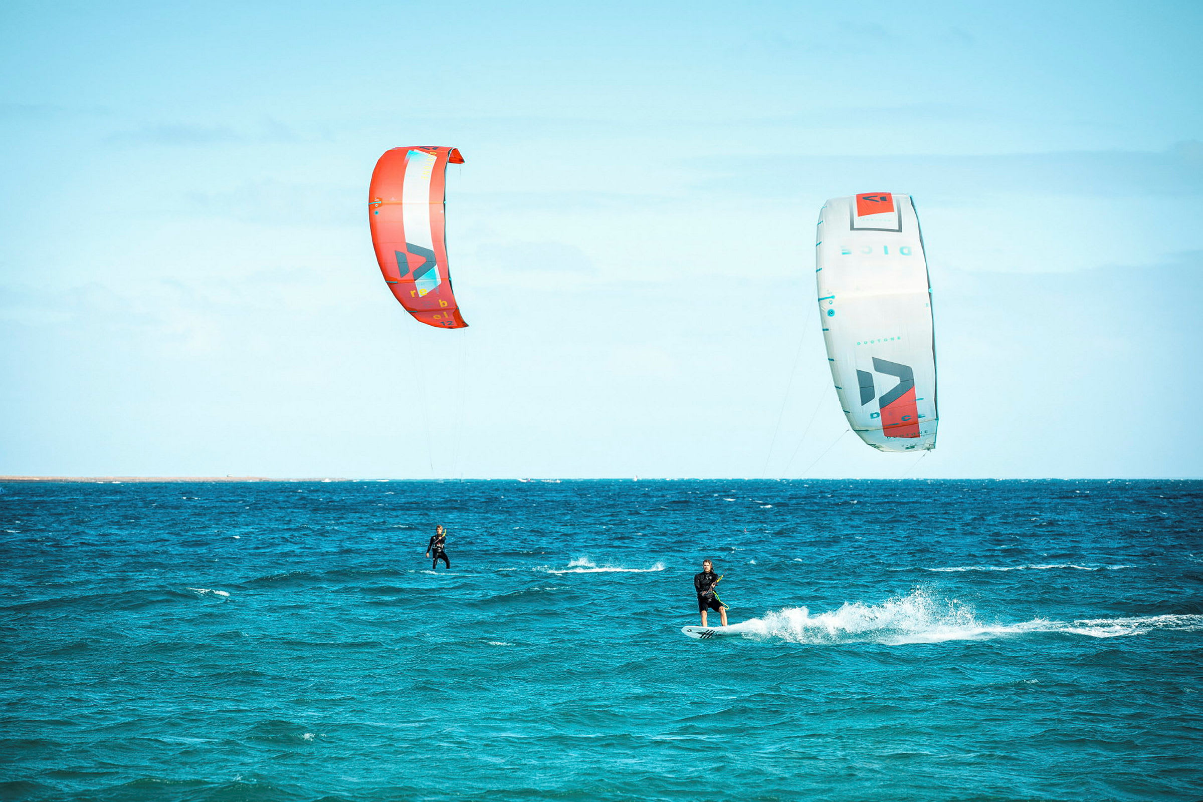 Kaksi henkilöä kitesurffaa merellä värikkäiden leijojen kanssa. (Tekoälyn luoma teksti)