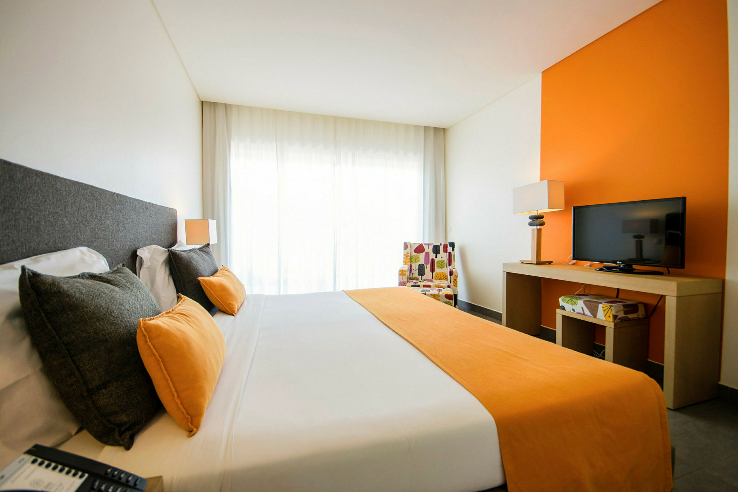 Kuva hotellihuoneesta, jossa parivuode, oransseja yksityiskohtia ja televisio pöydällä. (Tekoälyn luoma teksti)
