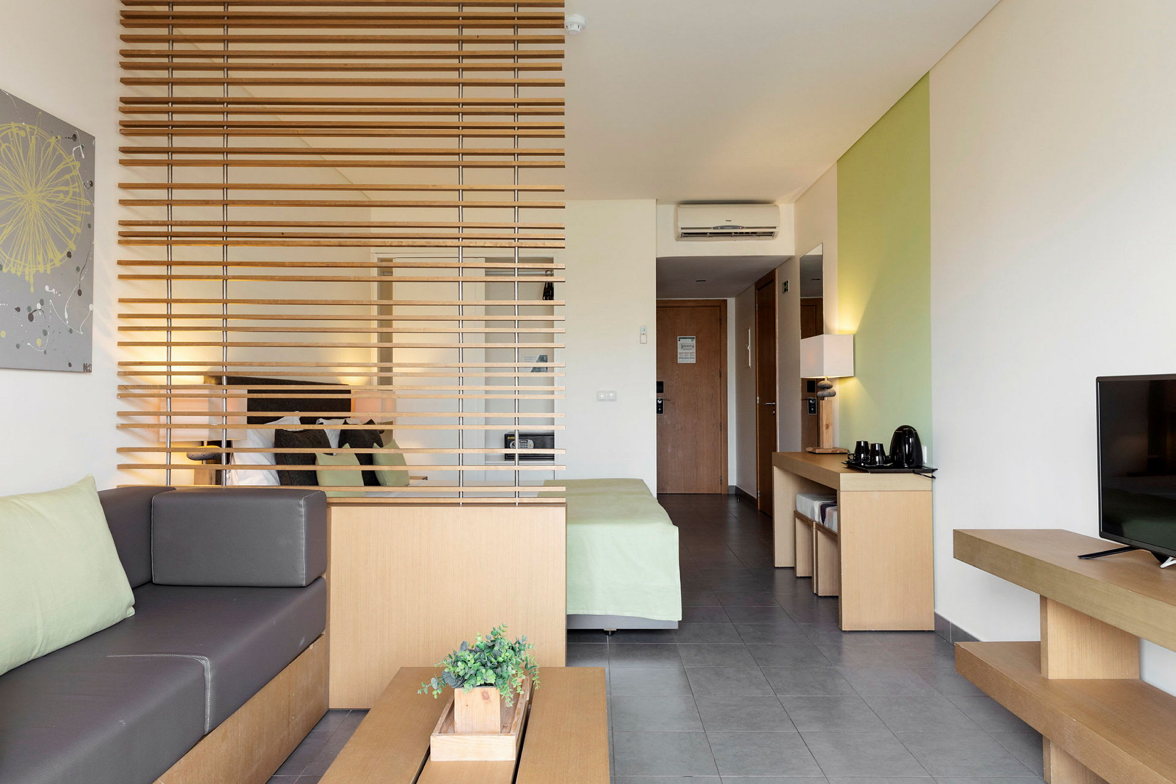 Moderni hotellihuone, jossa oleskelutila, sänky ja luonnonsävyisiä huonekaluja. (Tekoälyn luoma teksti)