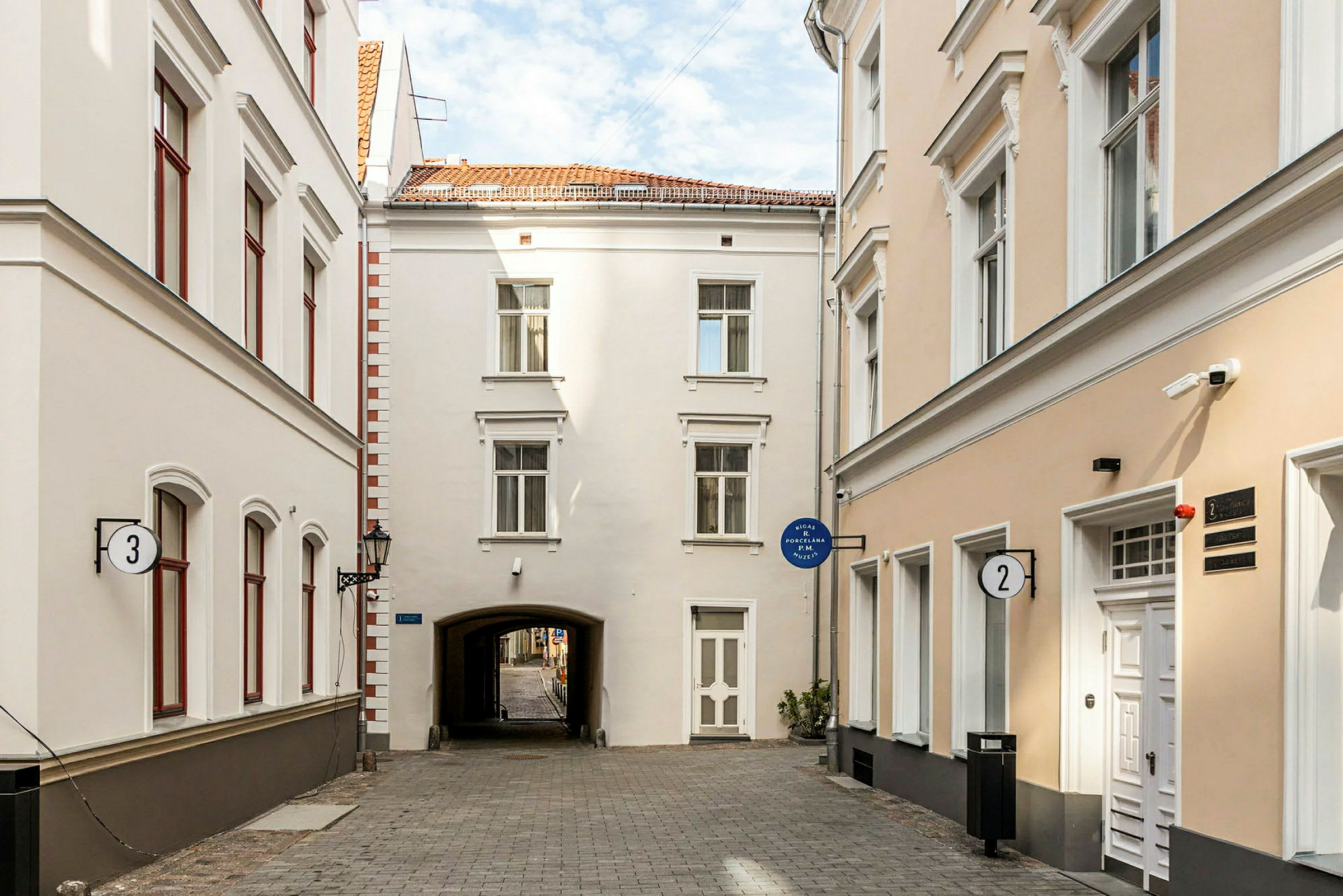 Kapea katu, jota ympäröivät vaaleat rakennukset ikkunoineen ja ovineen. (Tekoälyn luoma teksti)