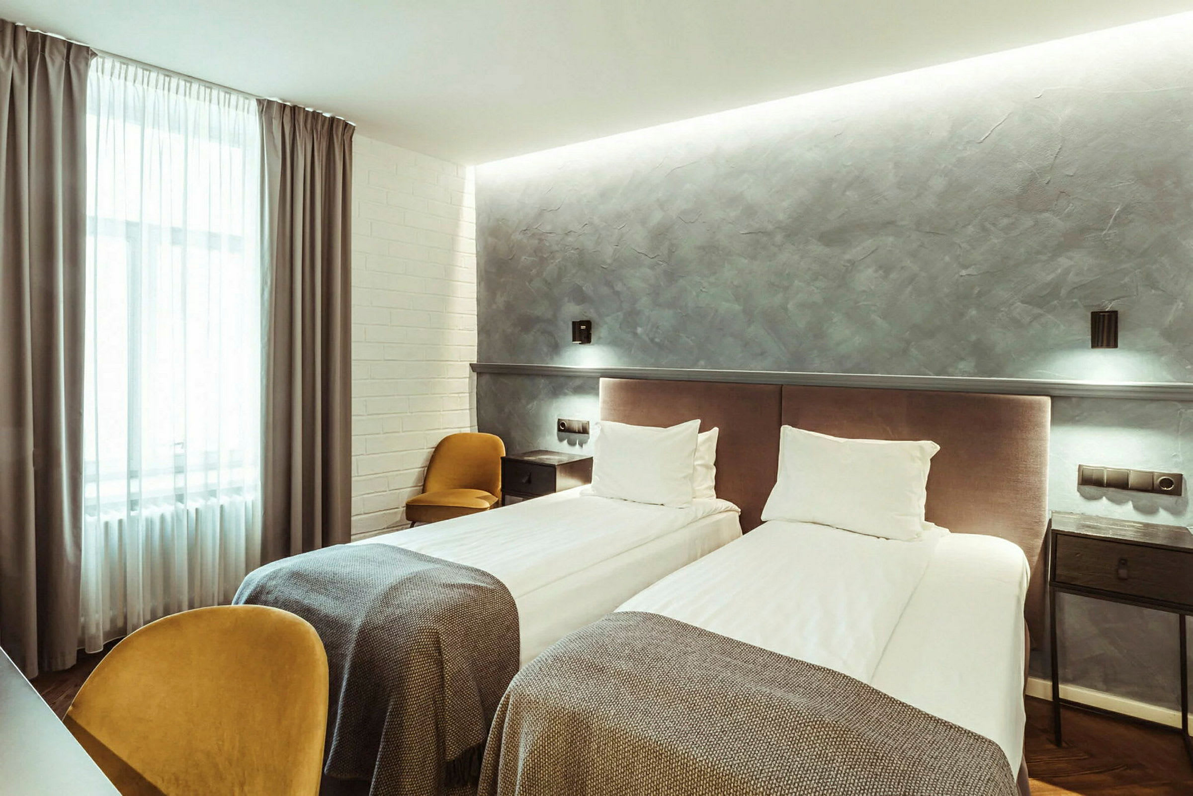 Hotellihuone, jossa on kaksi erillistä vuodetta, harmaa seinä ja suuri ikkunaverho. (Tekoälyn luoma teksti)