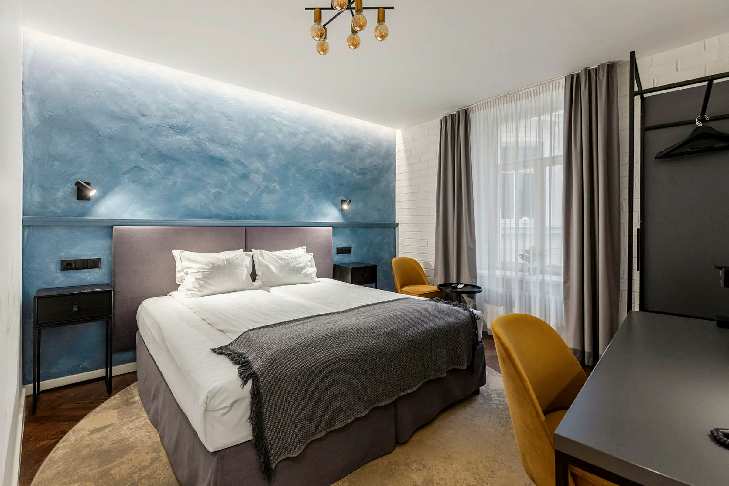 Hotellihuone, jossa on parivuode, sininen seinä ja keltaiset tuolit. (Tekoälyn luoma teksti)