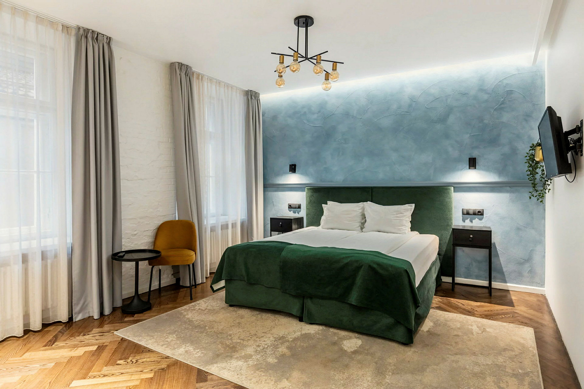 Tyylikäs hotellihuone, jossa on parivuode, sininen seinä ja vihreitä tekstiilejä. (Tekoälyn luoma teksti)