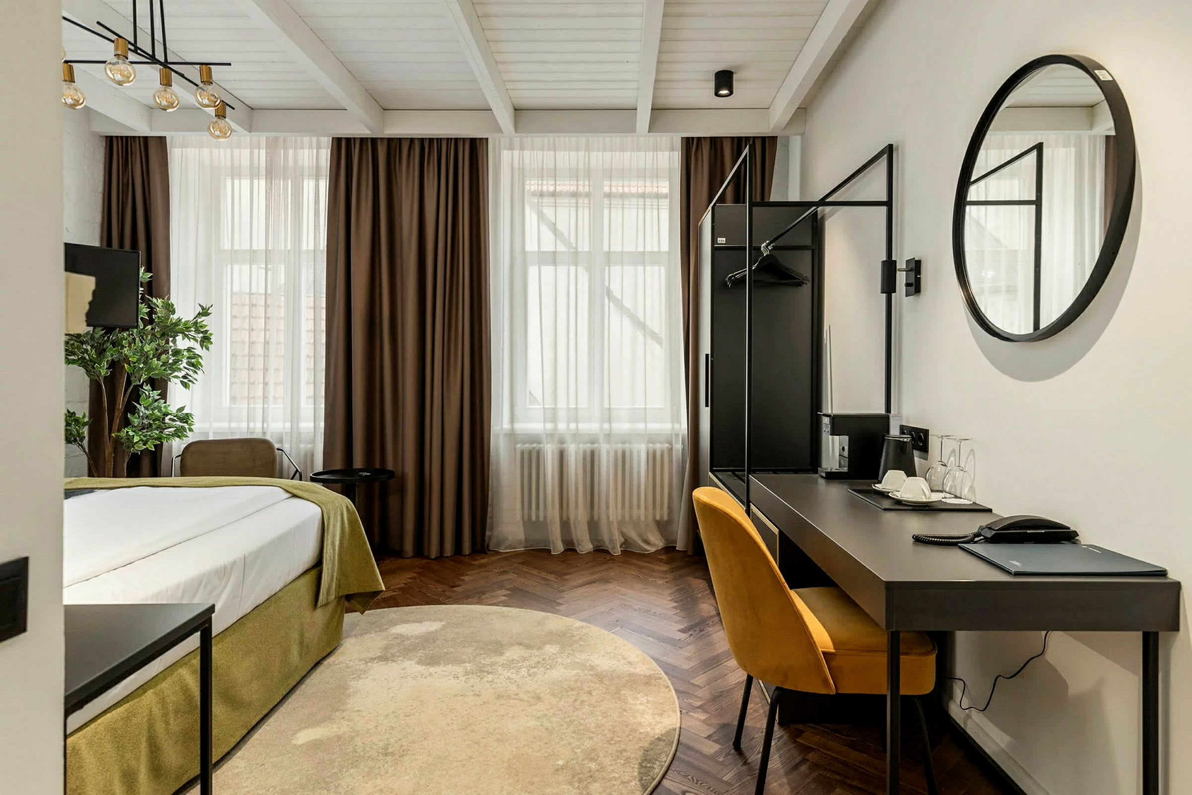 Moderni hotellihuone, jossa sänky, kirjoituspöytä ja keltainen tuoli. (Tekoälyn luoma teksti)