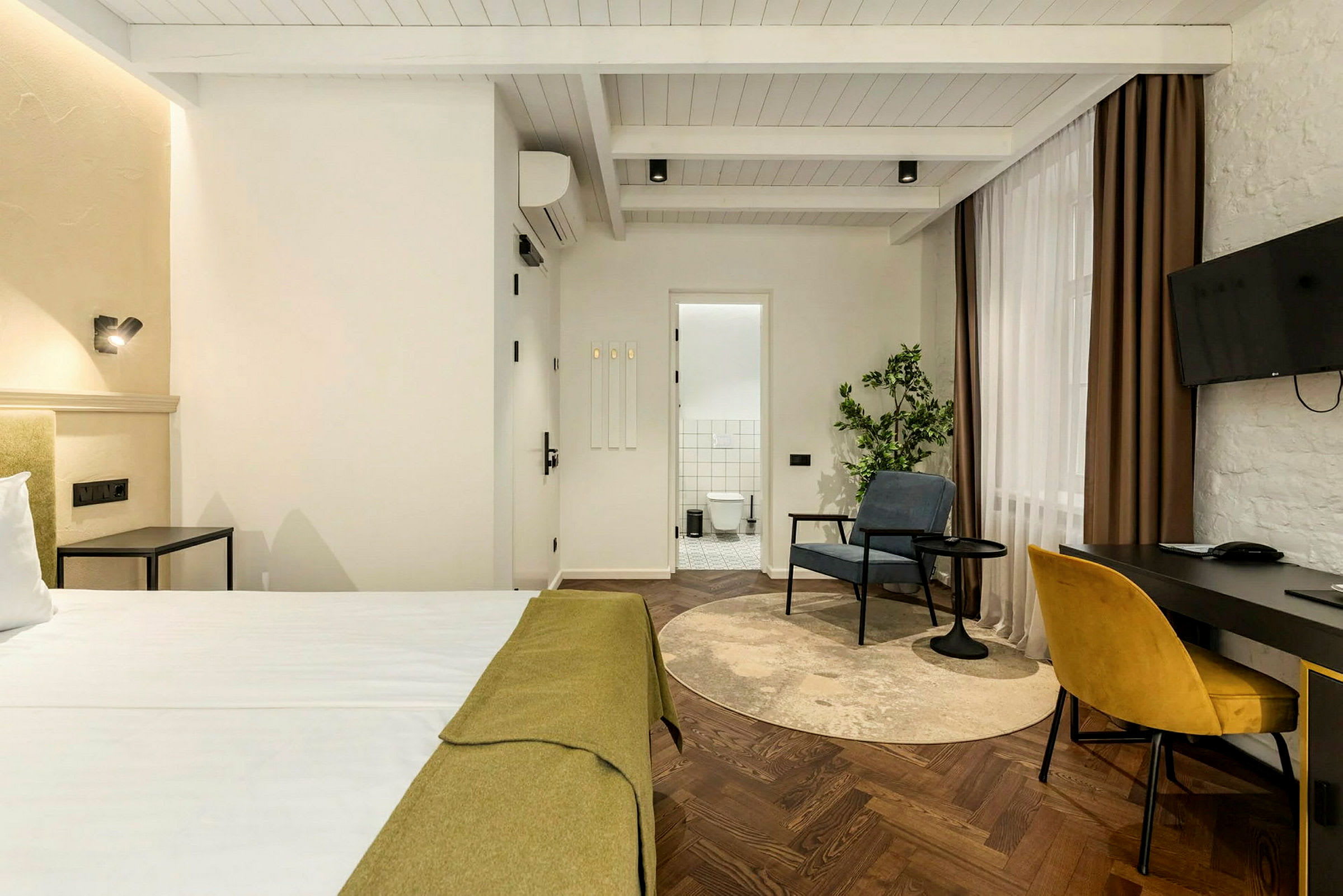 Hotellihuone, jossa on sänky, työpöytä tuoleineen, nojatuoli ja kylpyhuone taustalla. (Tekoälyn luoma teksti)