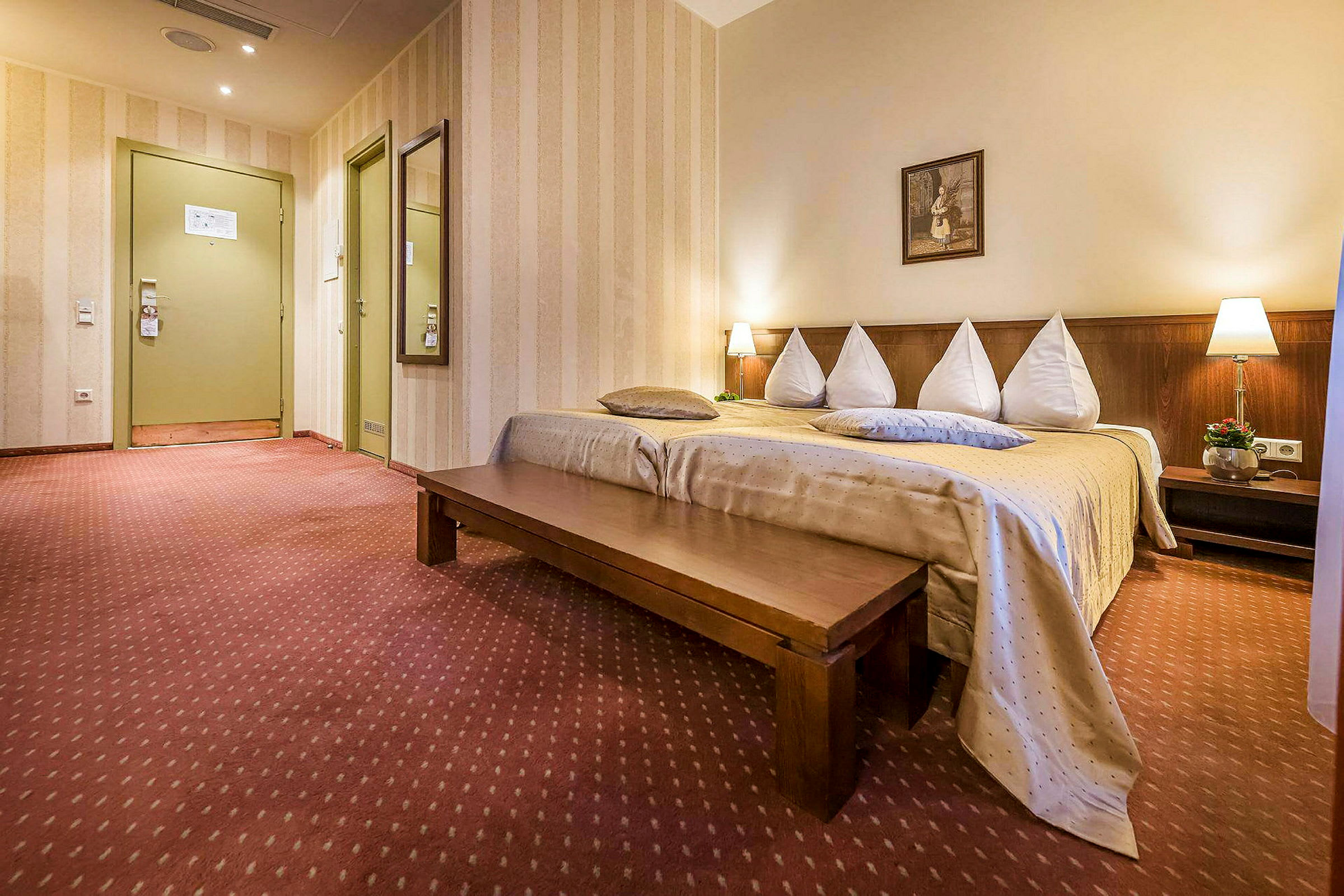Hotellihuone, jossa on sijattu sänky, pitkä puupenkki ja koristeelliset valaisimet. (Tekoälyn luoma teksti)