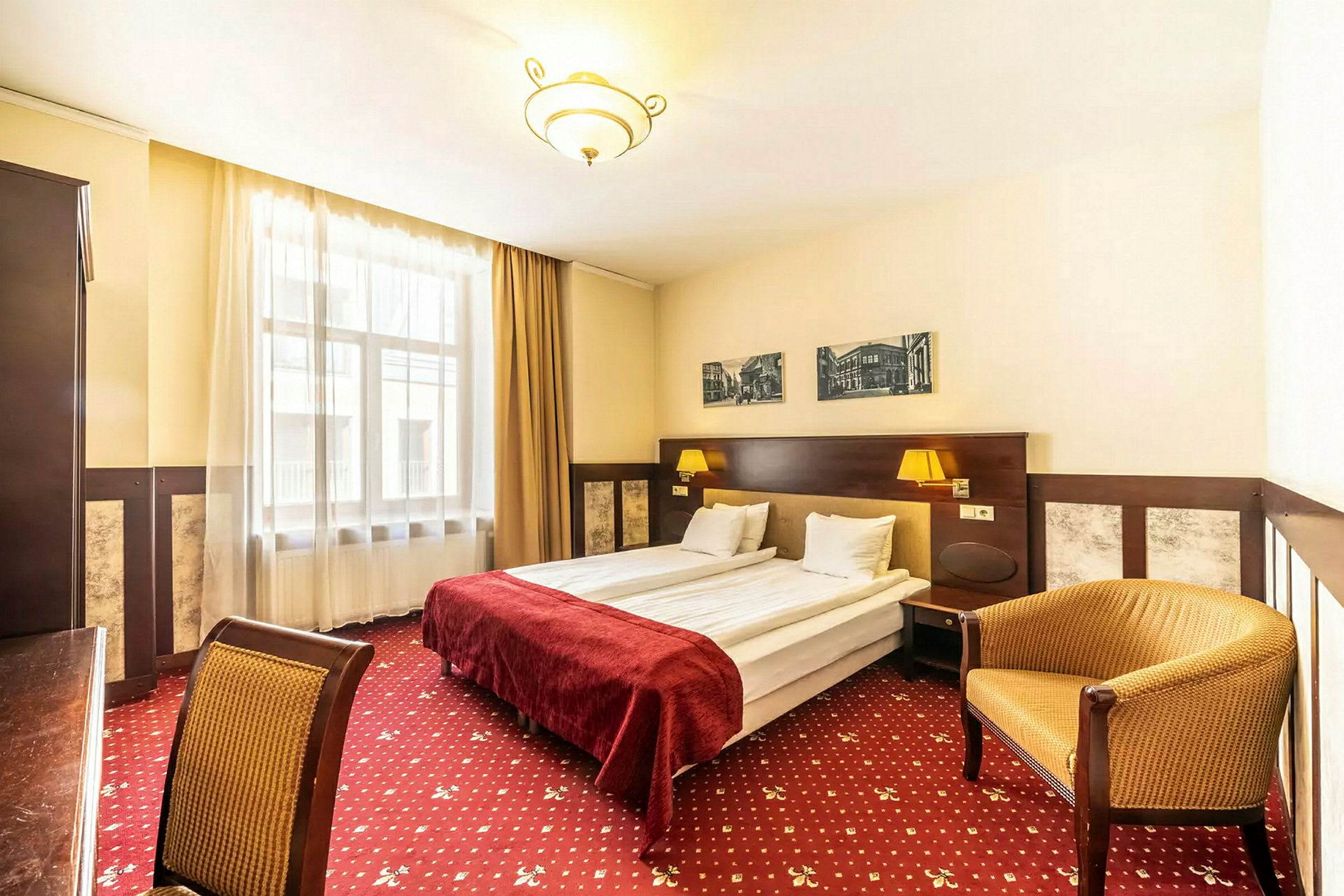 Hotellihuone, jossa on parivuode, punaiset vuodevaatteet, seinäkoristeita ja tuoleja. (Tekoälyn luoma teksti)