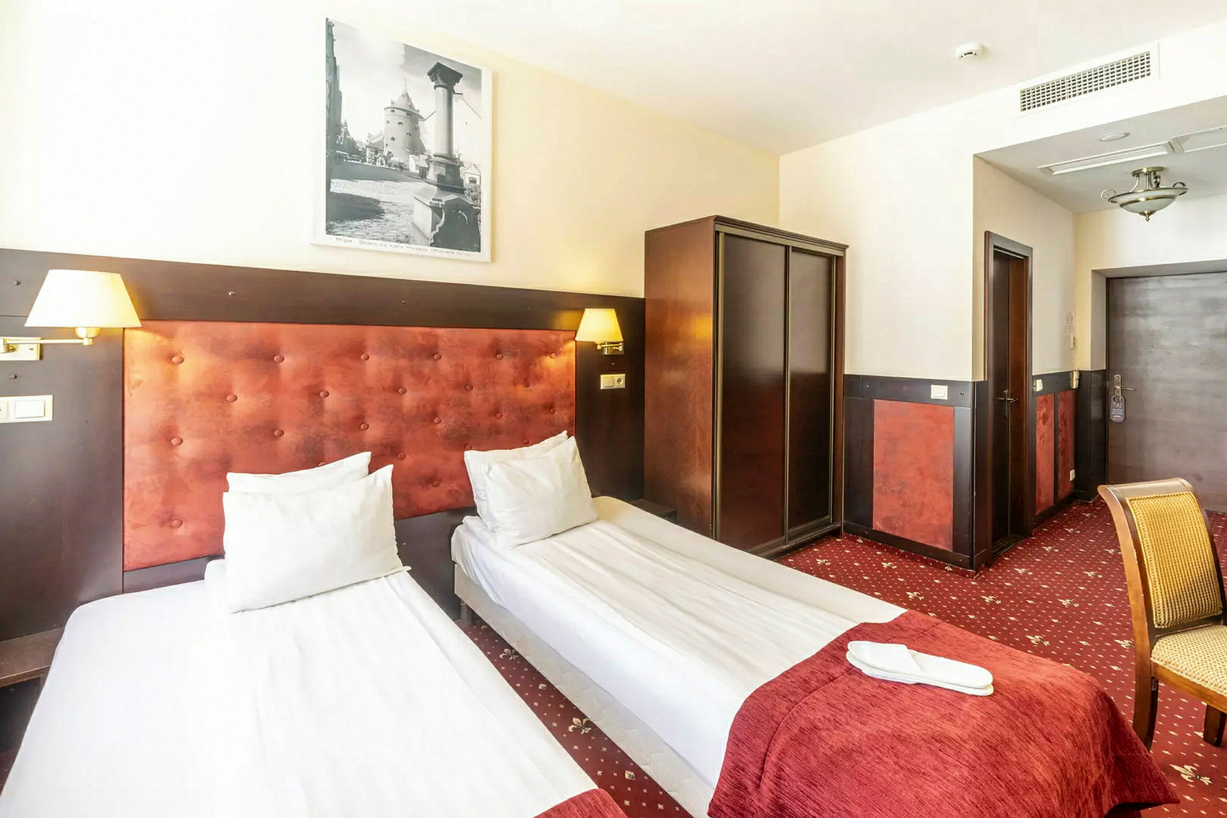 Hotellihuone, jossa on kaksi yhden hengen sänkyä, vaatekaappi ja tuoli. (Tekoälyn luoma teksti)