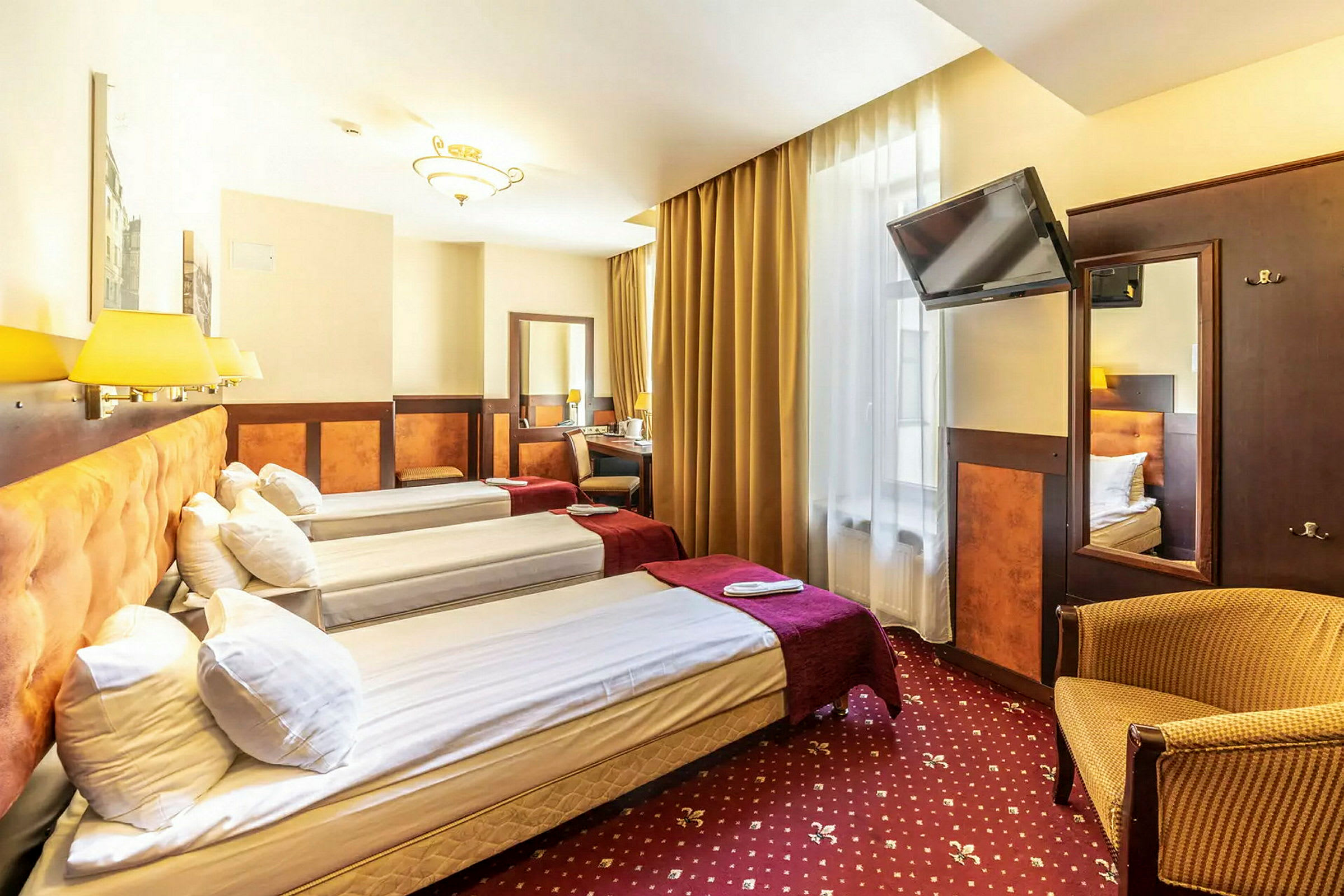 Hotellihuone, jossa kolme yhden hengen vuodetta, televisio, kirjoituspöytä ja nojatuoli. (Tekoälyn luoma teksti)