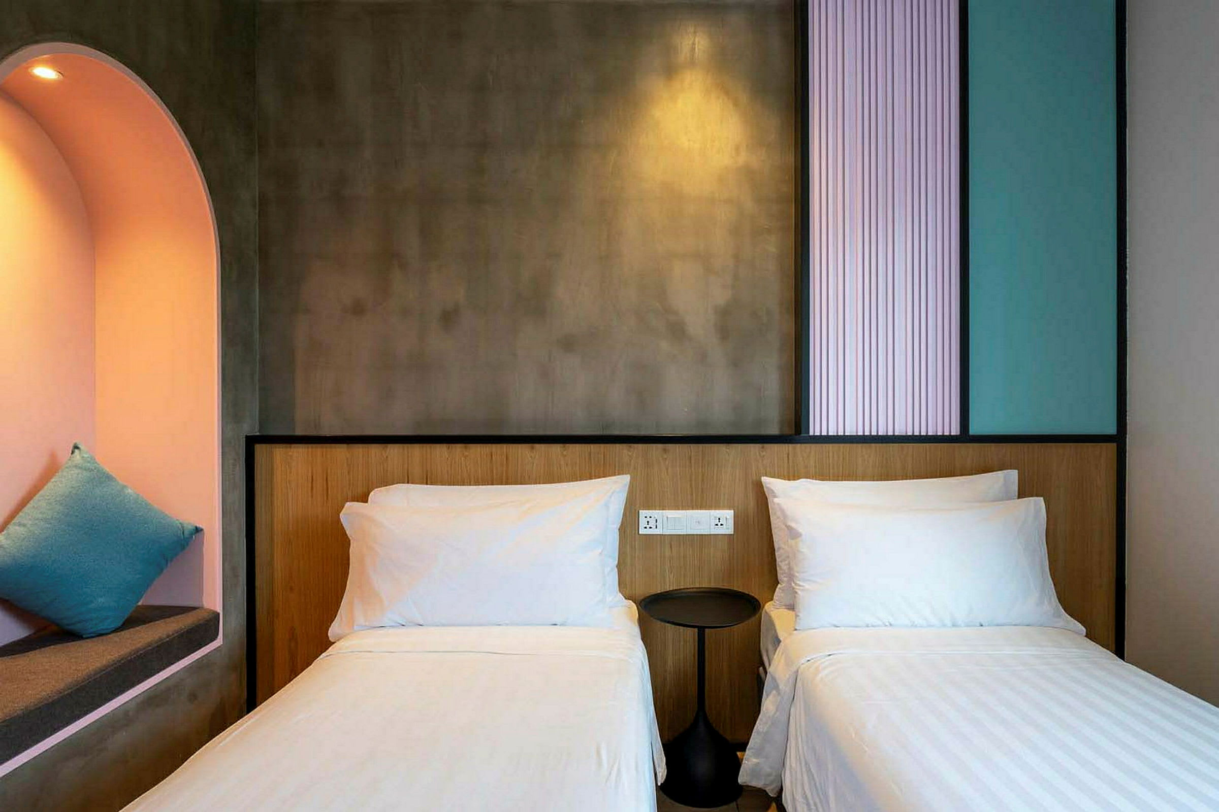 Hotellihuone, jossa on kaksi yhden hengen vuodetta, pieni pyöreä yöpöytä ja sisäänrakennettu syvennys, jossa tyyny. (Tekoälyn luoma teksti)