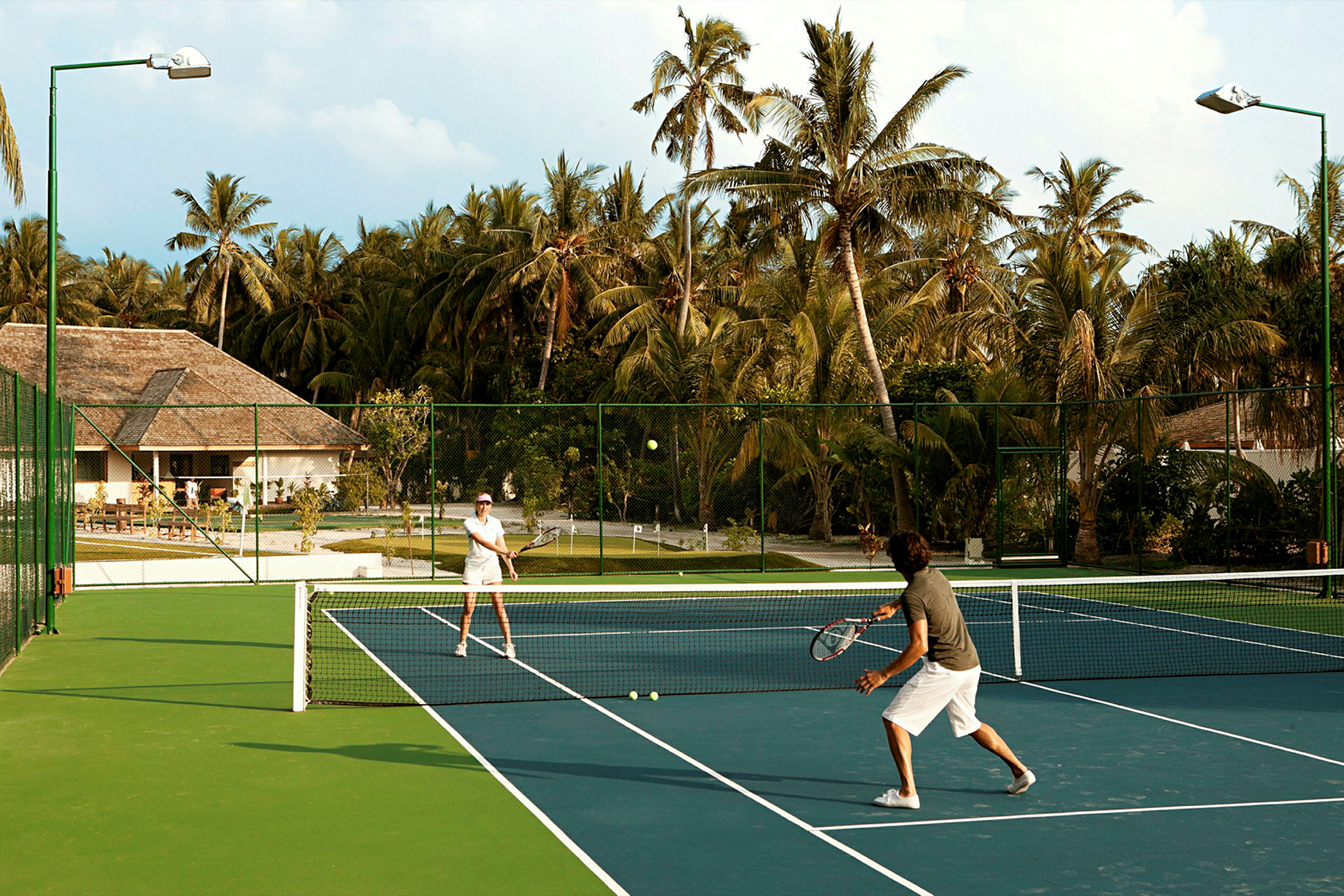 Kaksi ihmistä pelaa tennistä ulkokentällä palmuilla ympäröitynä. (Tekoälyn luoma teksti)