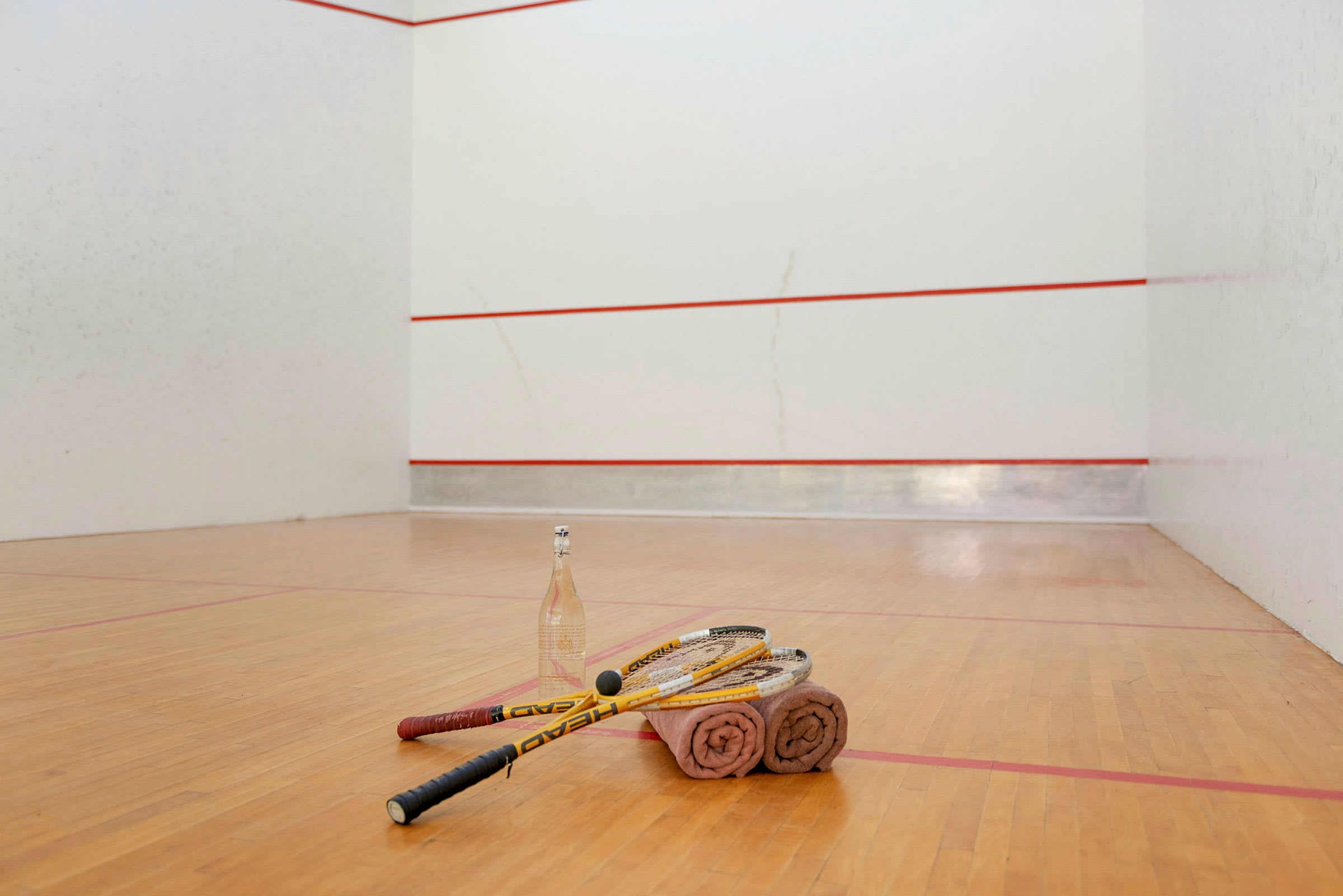 Squash-mailat, pyyhkeet ja vesipullo ovat lattialla squash-kentällä. (Tekoälyn luoma teksti)