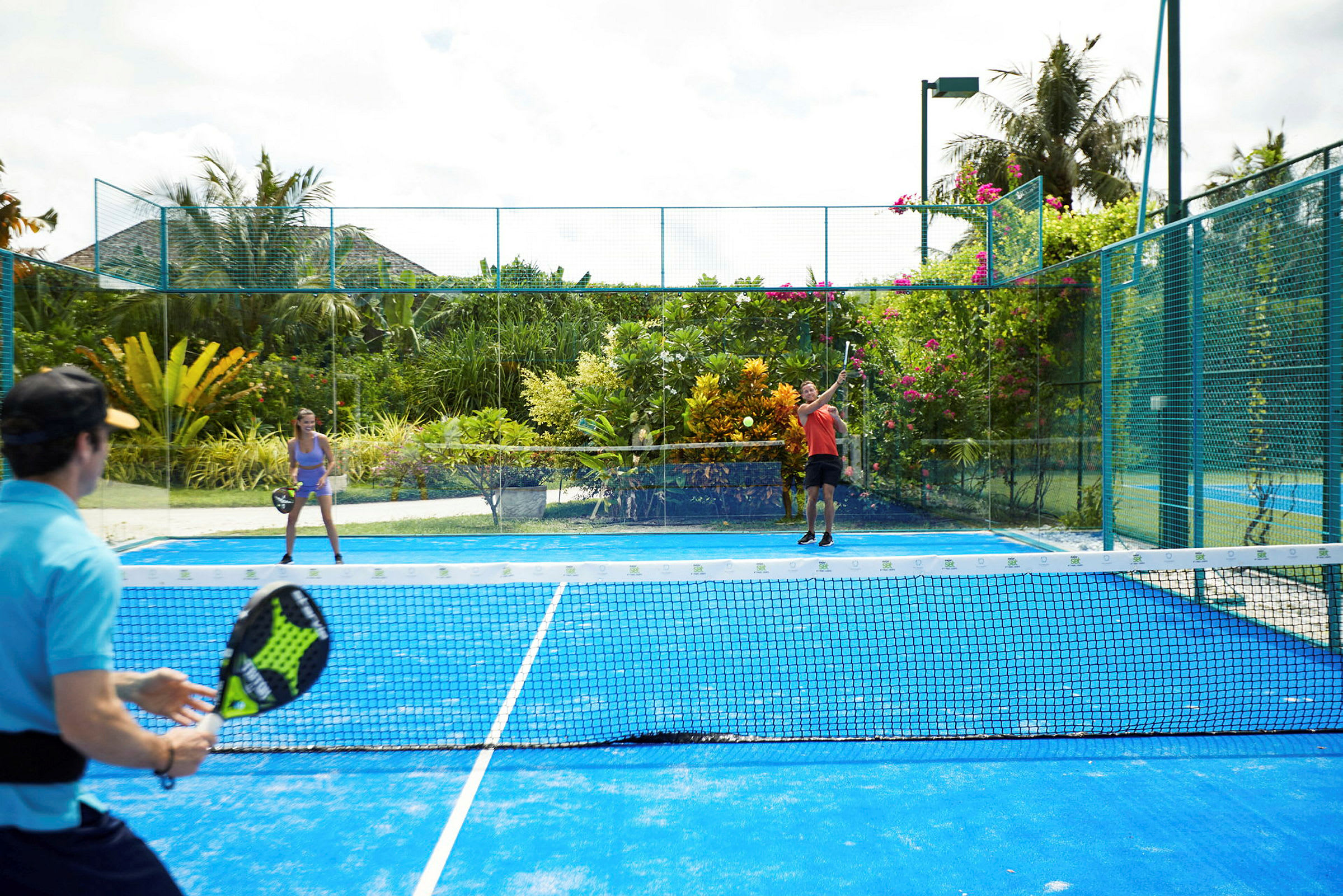 Henkilöt pelaavat padelia ulkokentällä vehreän kasvillisuuden ympäröimänä. (Tekoälyn luoma teksti)