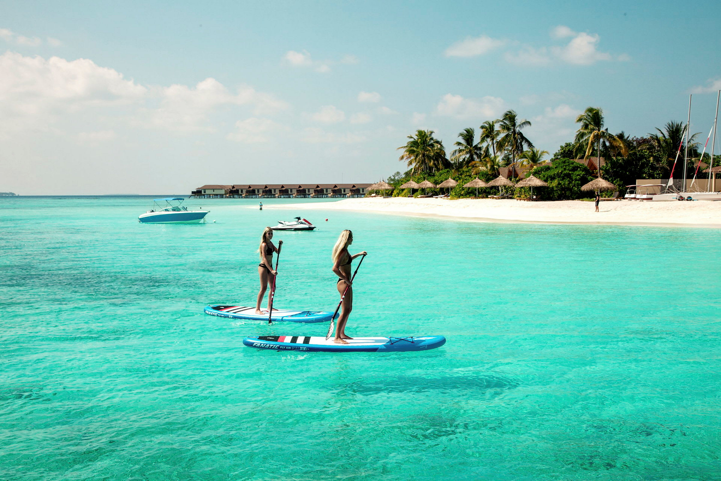 Kaksi henkilöä seisoo paddleboardeilla kirkkaassa turkoosissa vedessä lähellä hiekkarantaa. (Tekoälyn luoma teksti)