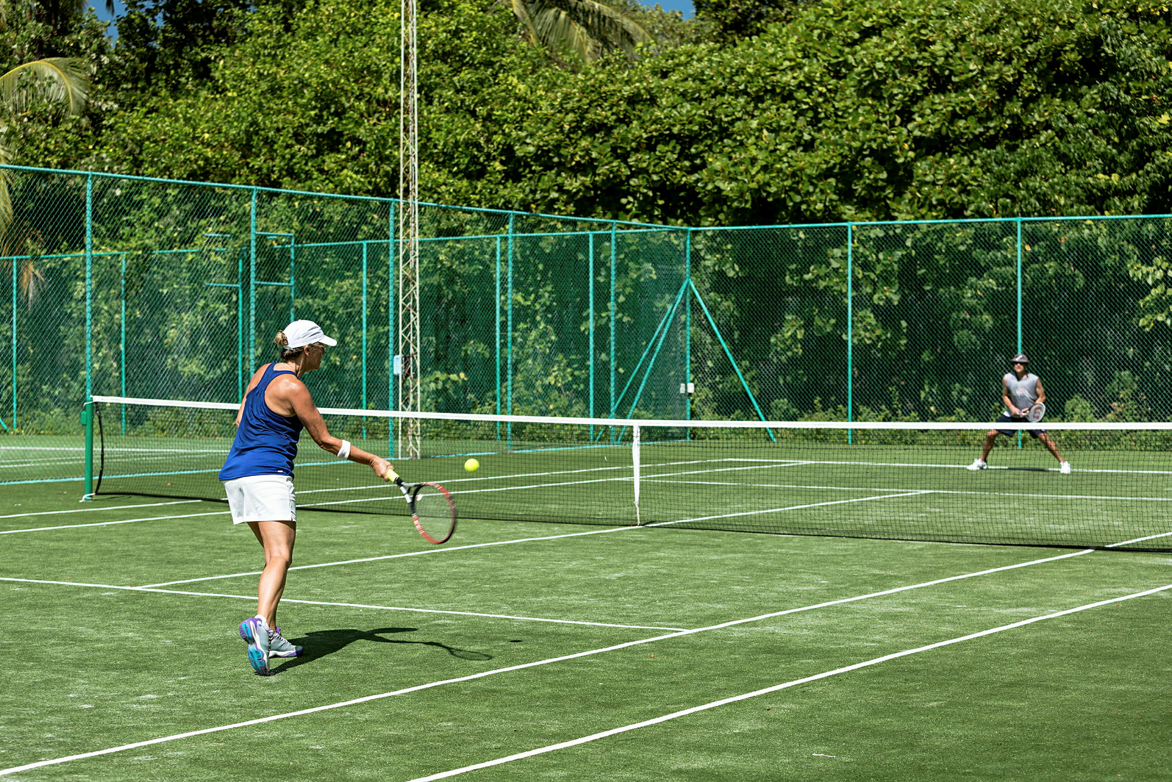 Henkilö pelaa tennistä vihreällä tennisalueella, jota ympäröi vehreä ympäristö. (Tekoälyn luoma teksti)