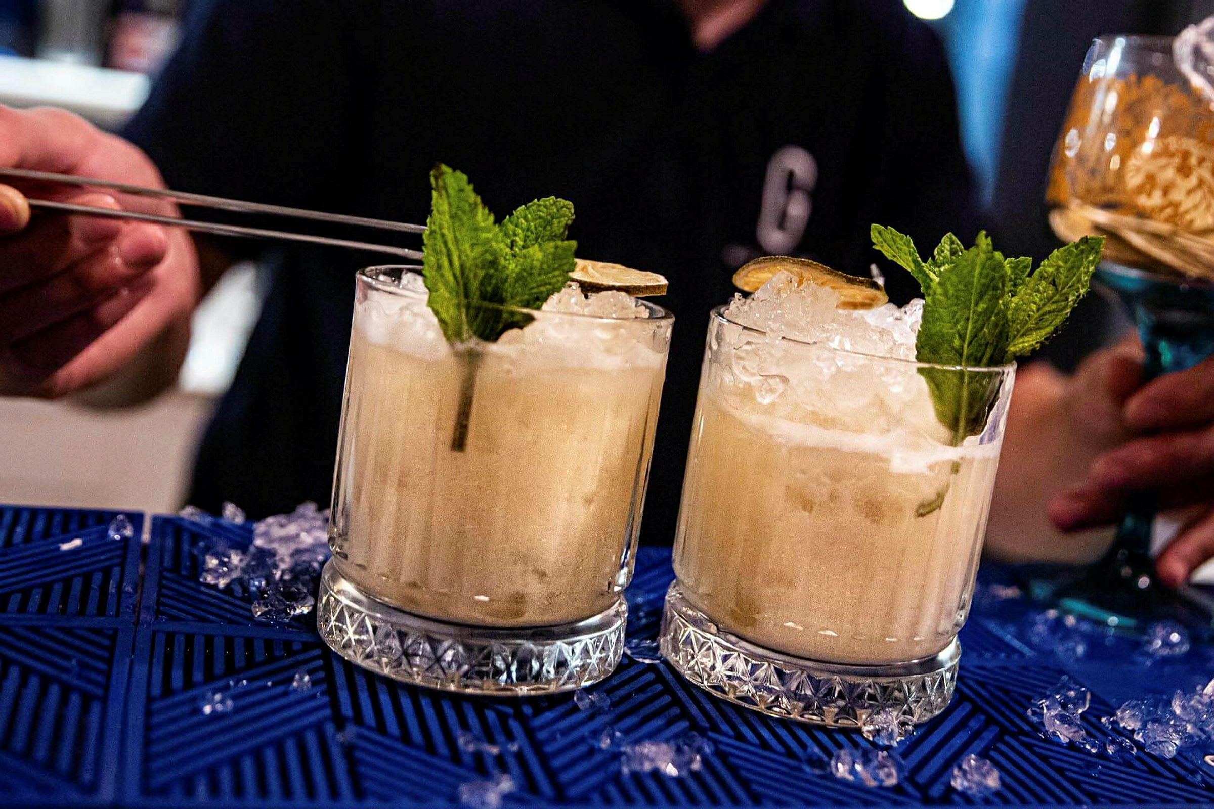 Kaksi cocktailia jäällä, mintulla ja limellä sinisellä pöytäliinalla. (Tekoälyn luoma teksti)