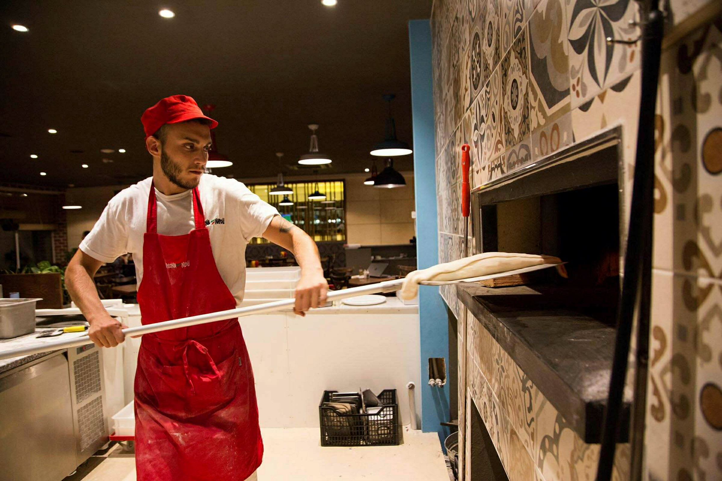 Kokki työvaatteissa valmistaa pizzaa ja asettaa sen puu-uunin sisään. (Tekoälyn luoma teksti)