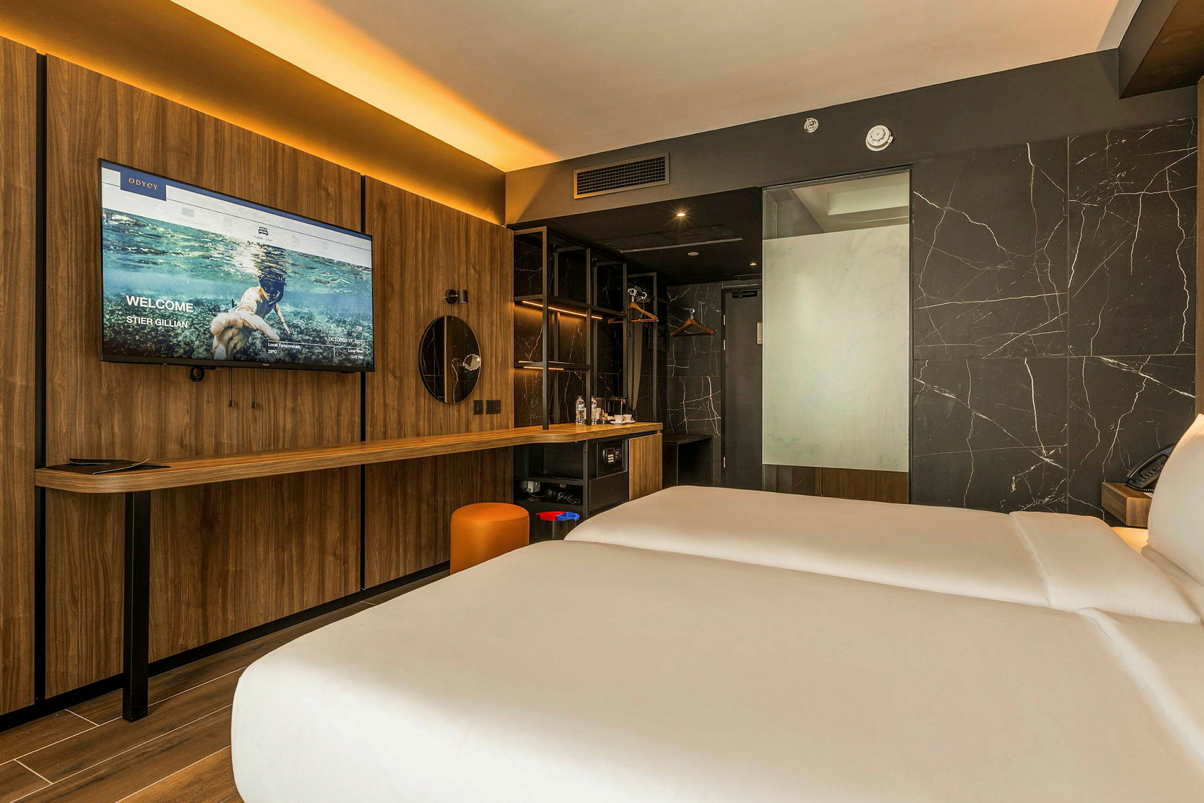 Moderni hotellihuone, jossa on kaksi vuodetta, puupaneeli, suuri televisio ja peili, työpöytä ja marmoriosein koristeltu seinä. (Tekoälyn luoma teksti)