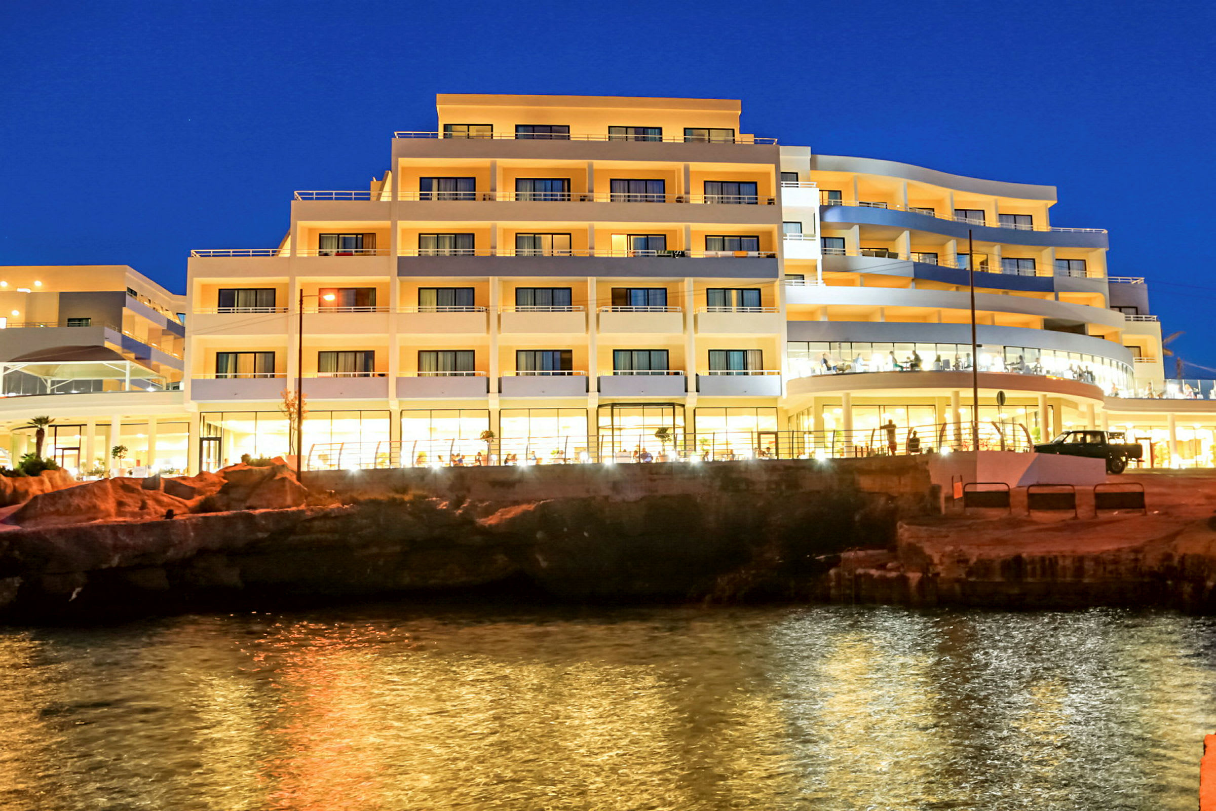 Hotellirakennus rannalla illalla, valot heijastuvat veteen. (Tekoälyn luoma teksti)