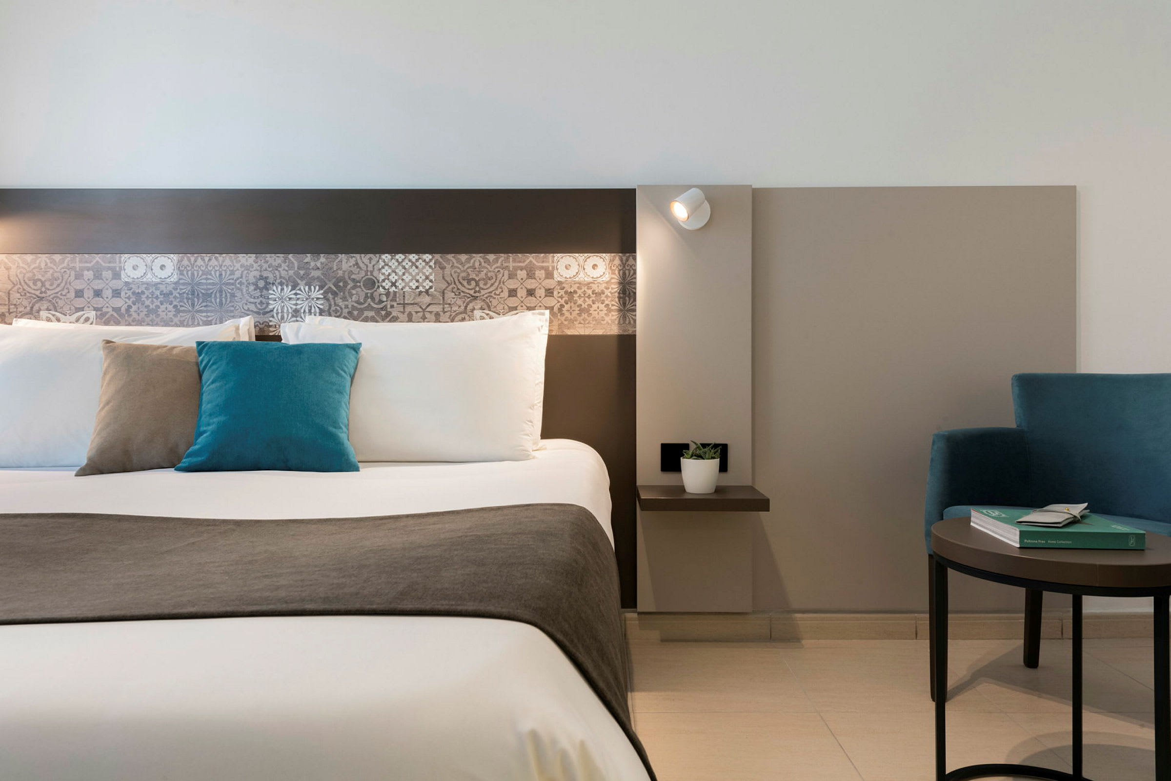 Kuva hotellihuoneen modernista sisustuksesta, jossa on pedattu sänky ja sininen nojatuoli. (Tekoälyn luoma teksti)