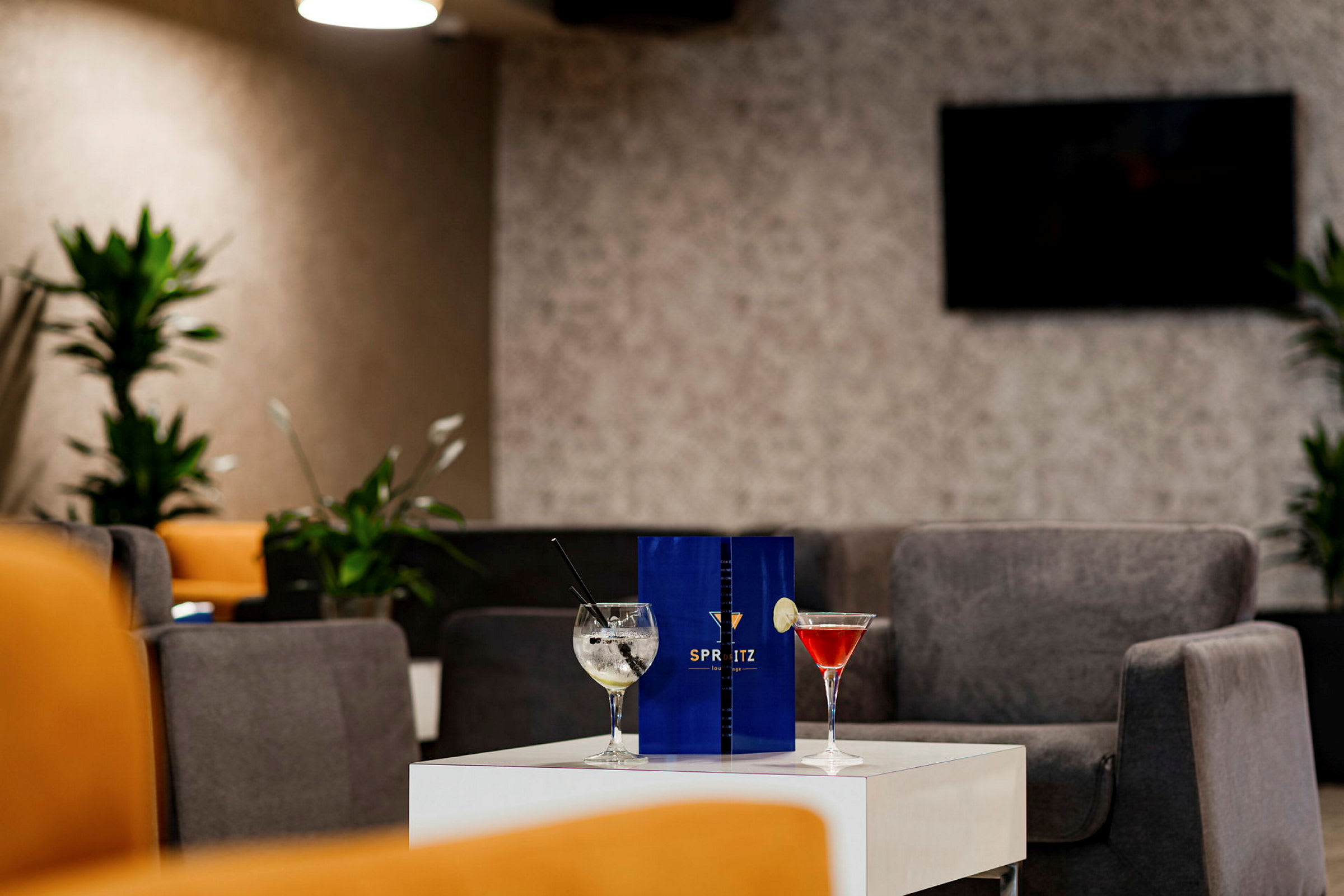Pöytä modernissa loungessa, jota ympäröivät mukavat istumapaikat, päällä kaksi cocktail-lasia ja ruokalista. (Tekoälyn luoma teksti)