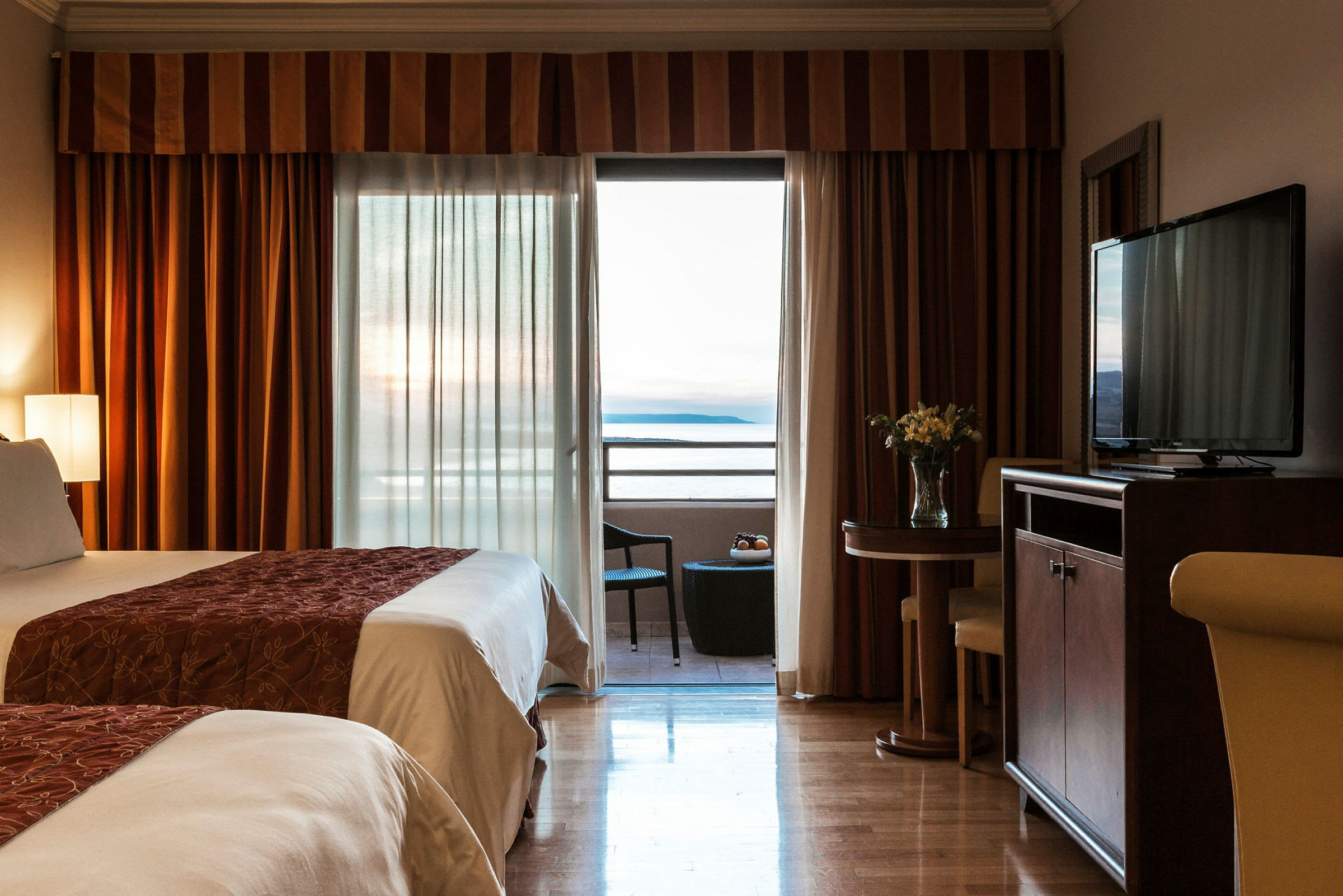Hotellihuone, jossa on kaksi sänkyä, parveke merinäköalalla ja pieni pöytä tuoleineen. (Tekoälyn luoma teksti)