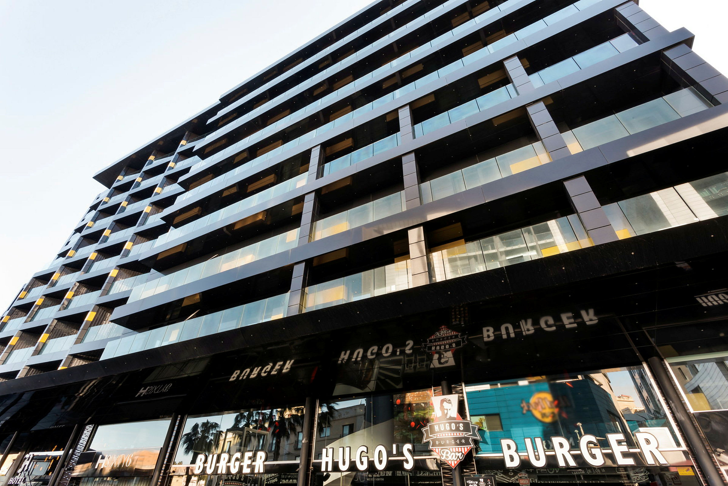 Moderni rakennus, jossa on lasi- ja metallijulkisivu sekä kylttejä Hugo's Burger -nimisestä hampurilaisravintolasta. (Tekoälyn luoma teksti)