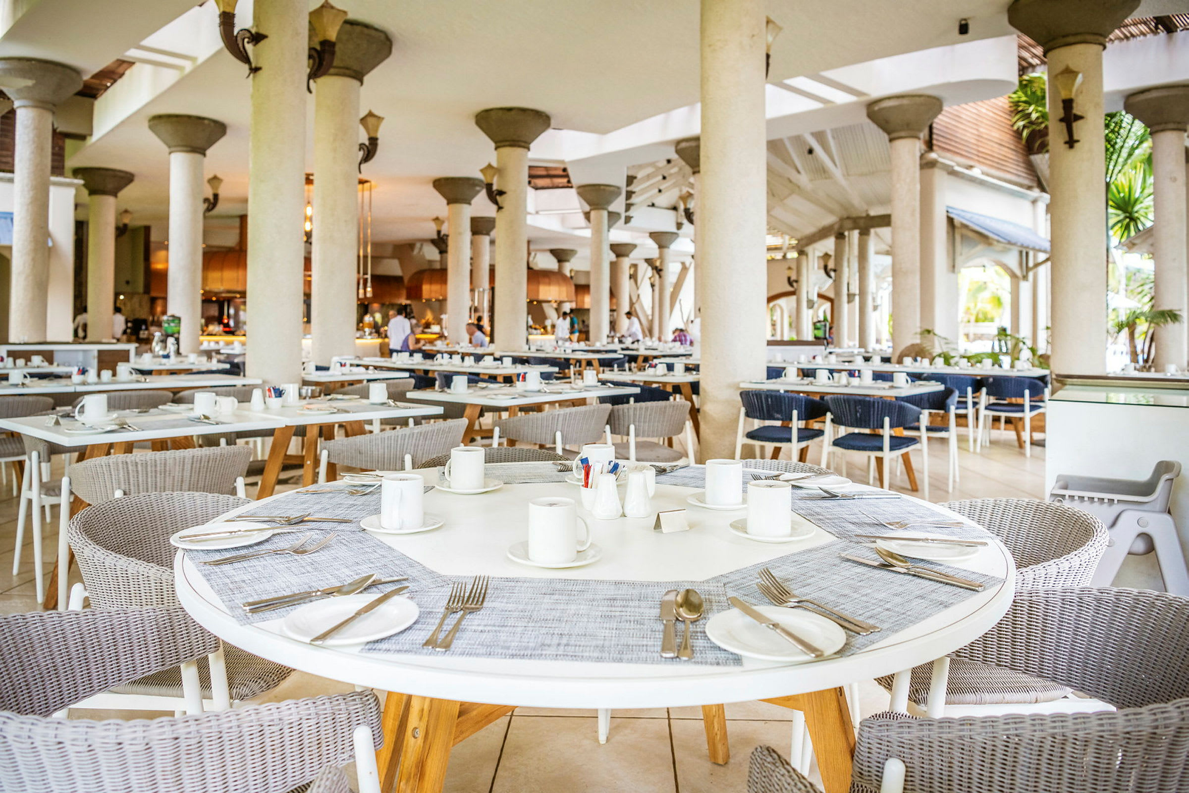 Avaran näköinen ravintola-alue, jossa pyöreitä pöytiä, tuoleja ja katettuja paikkoja. (Tekoälyn luoma teksti)