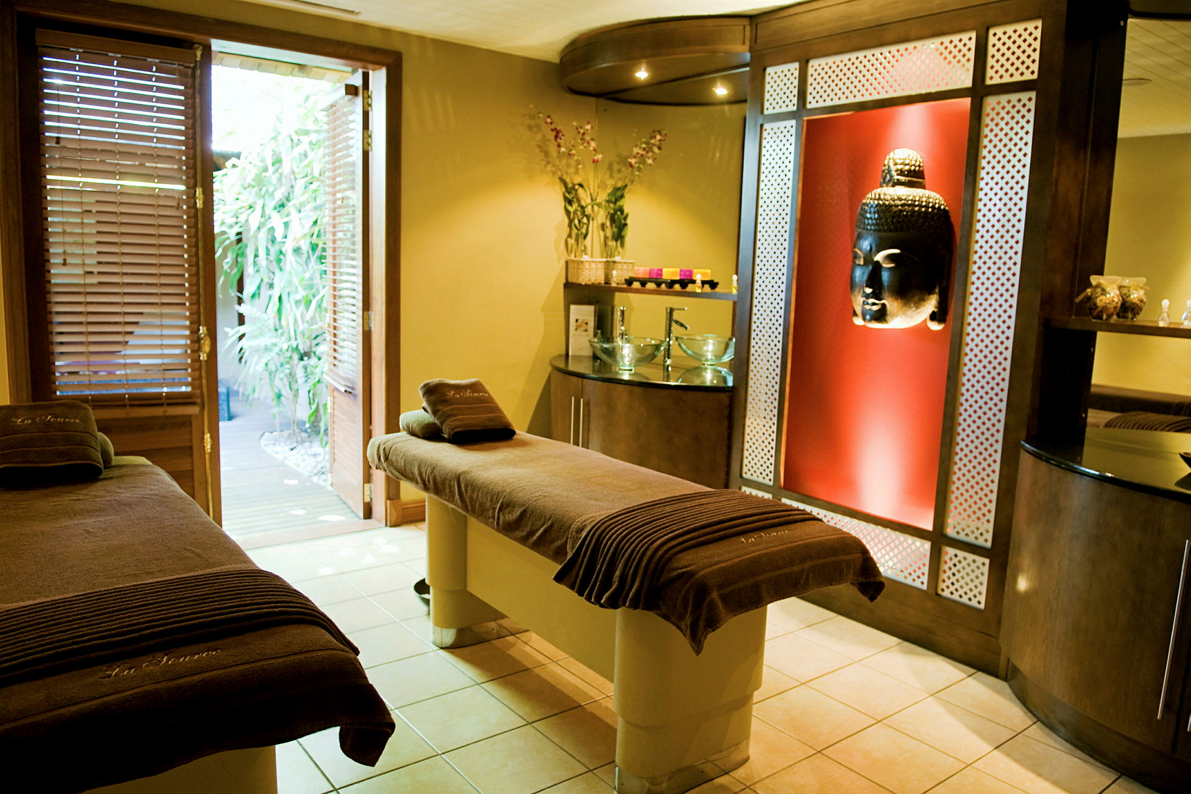 Spa-huone, jossa hierontapöytiä, Buddha-koriste ja avoin ovi puutarhaan. (Tekoälyn luoma teksti)